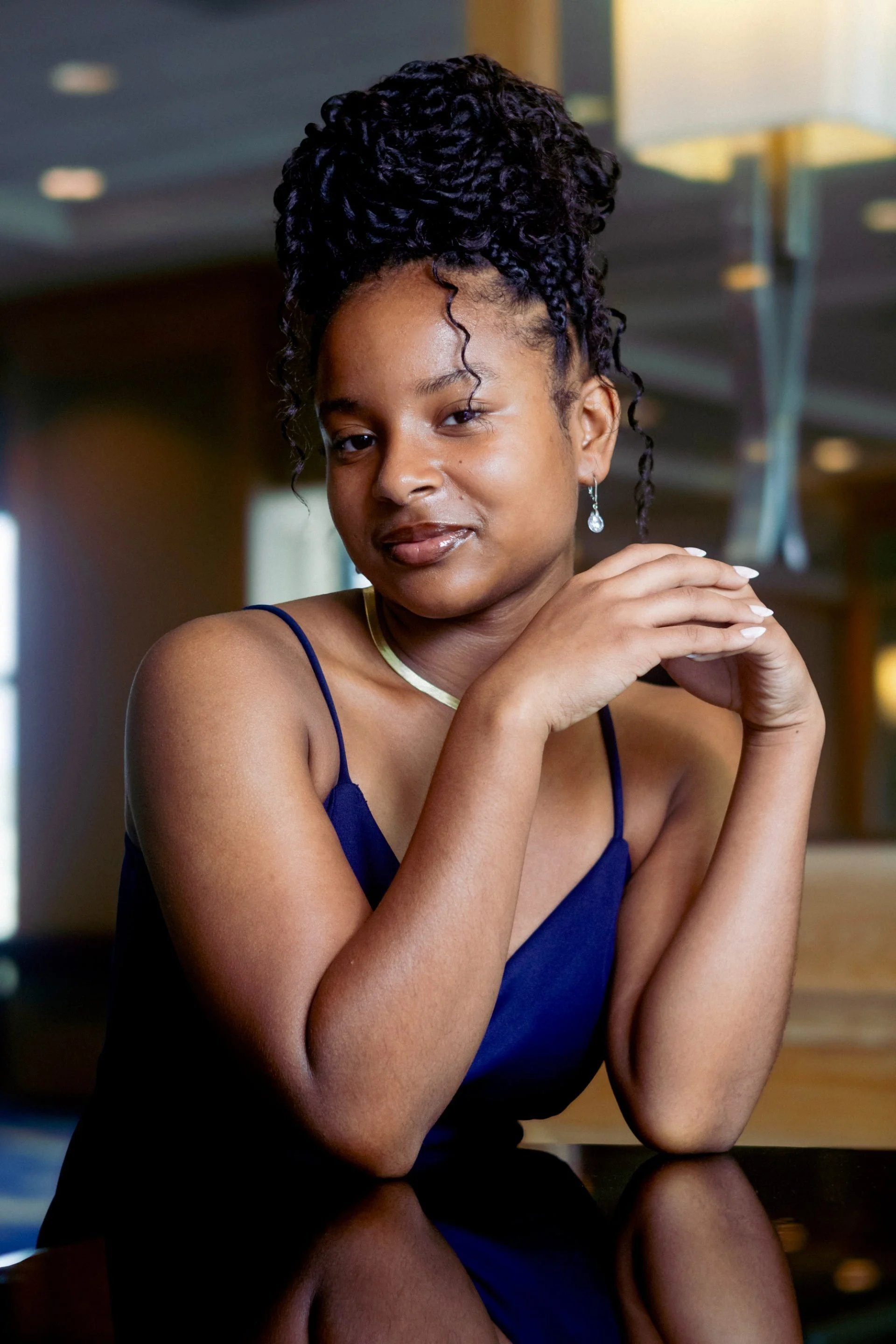 Jahneen Alexander in a navy blue dress, resting her elbows on a table with her hands clasped near her face.