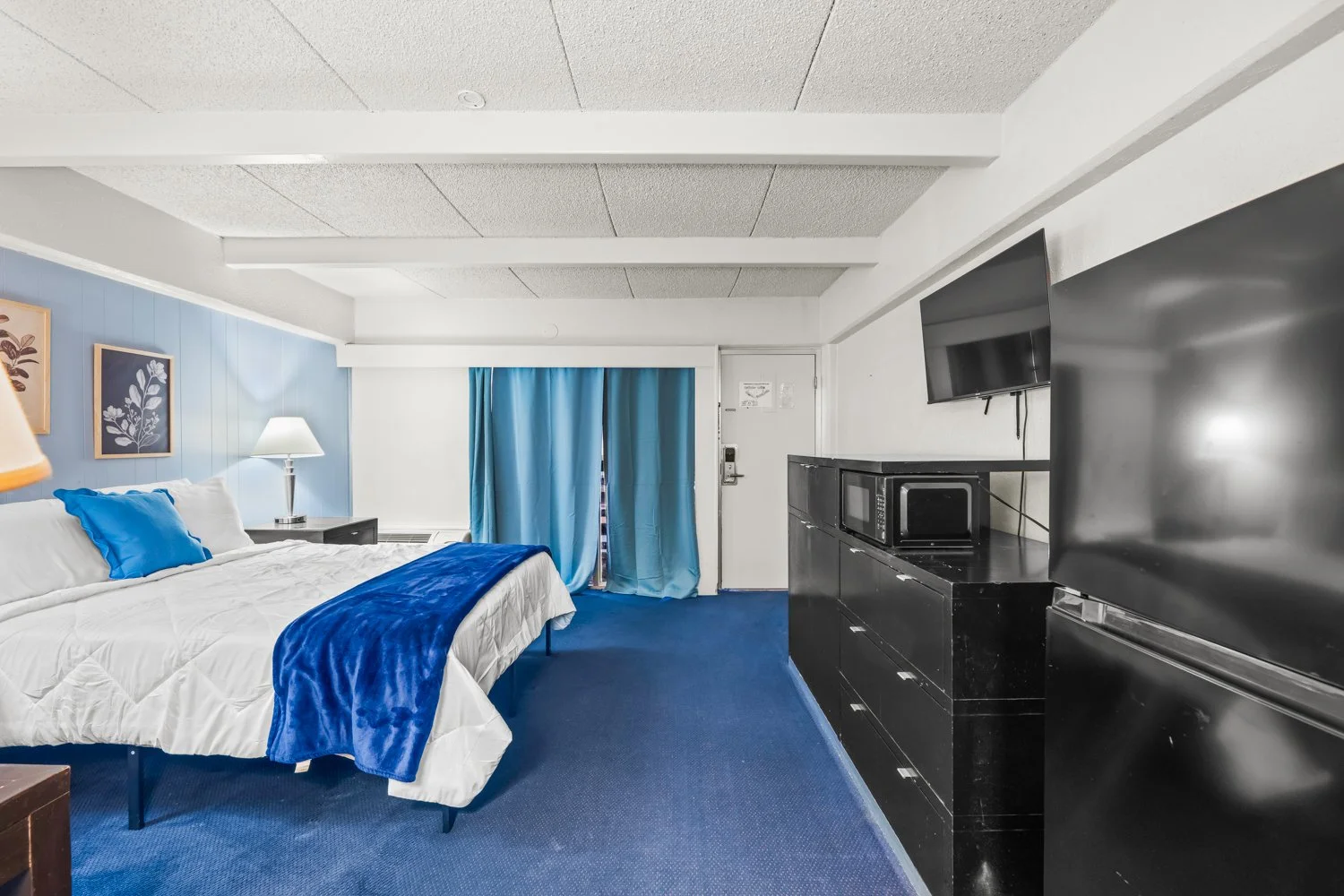 Room with bed, blue accents, a TV, a microwave, and curtains in a hotel room.