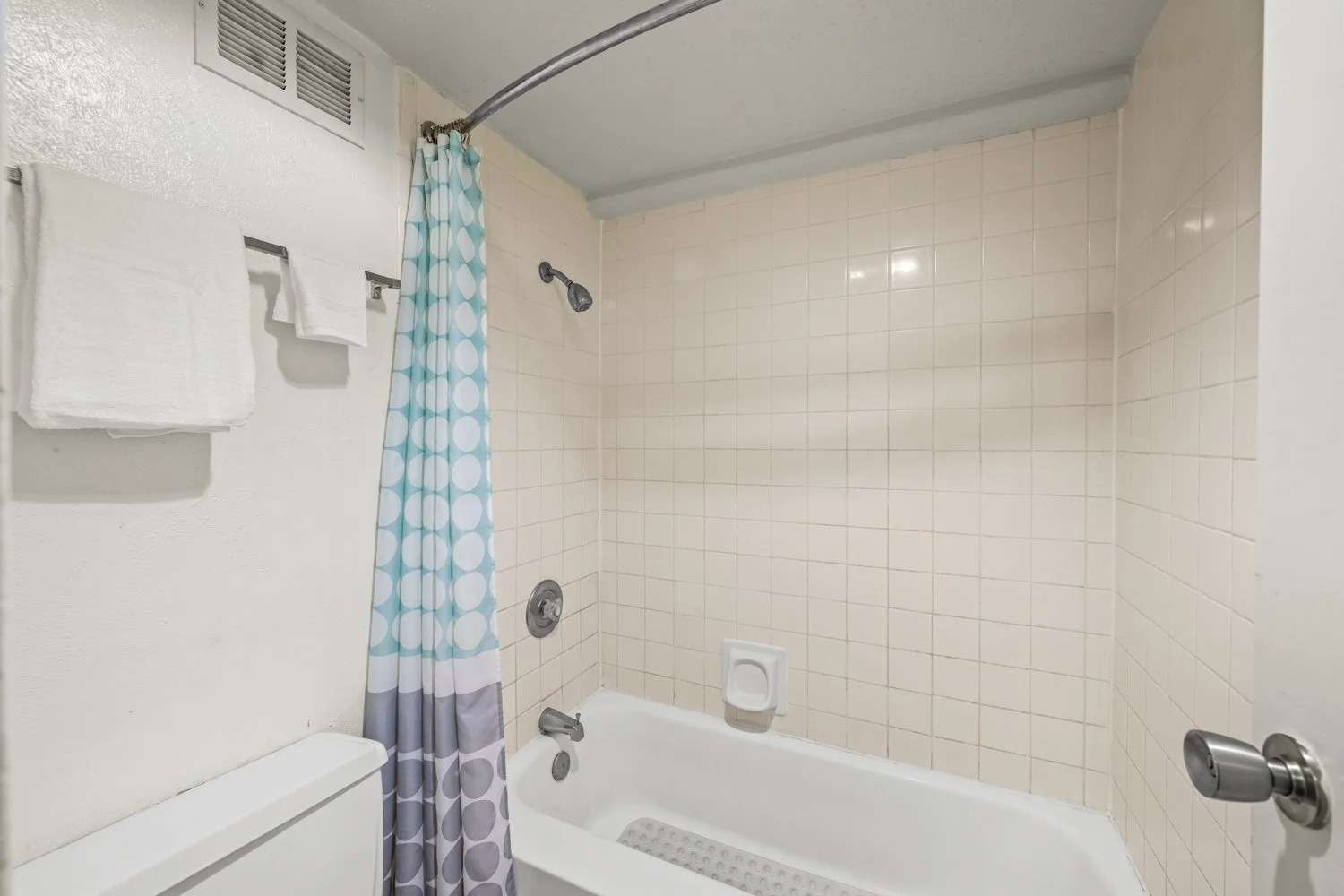 Bathroom shower area with beige tiled walls, a white bathtub, a blue and white polka dot shower curtain, a wall-mounted showerhead, and a white soap dish in the tub.