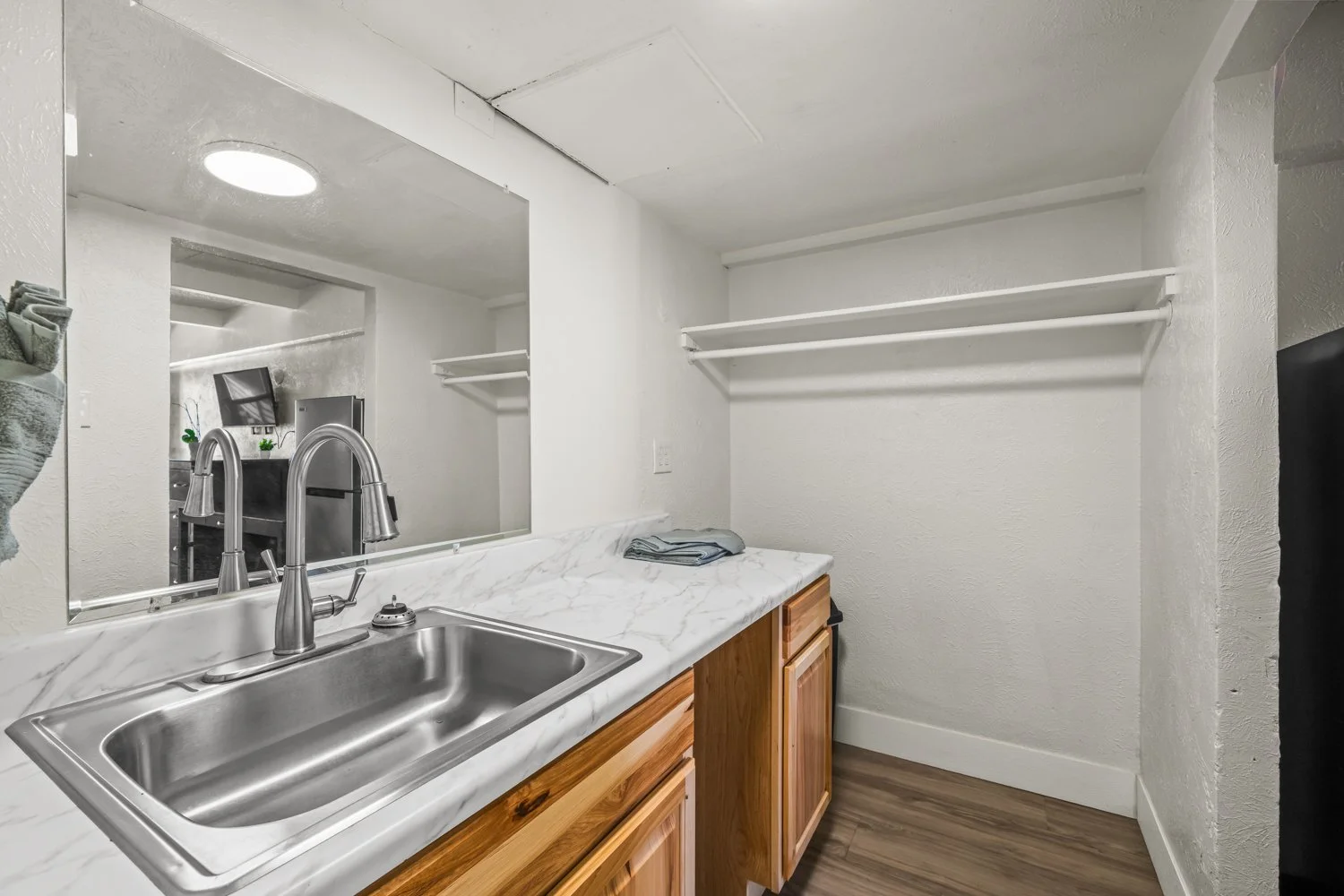 Small laundry or utility room with a stainless steel sink, wooden cabinets, a marble countertop, and white wall shelves.