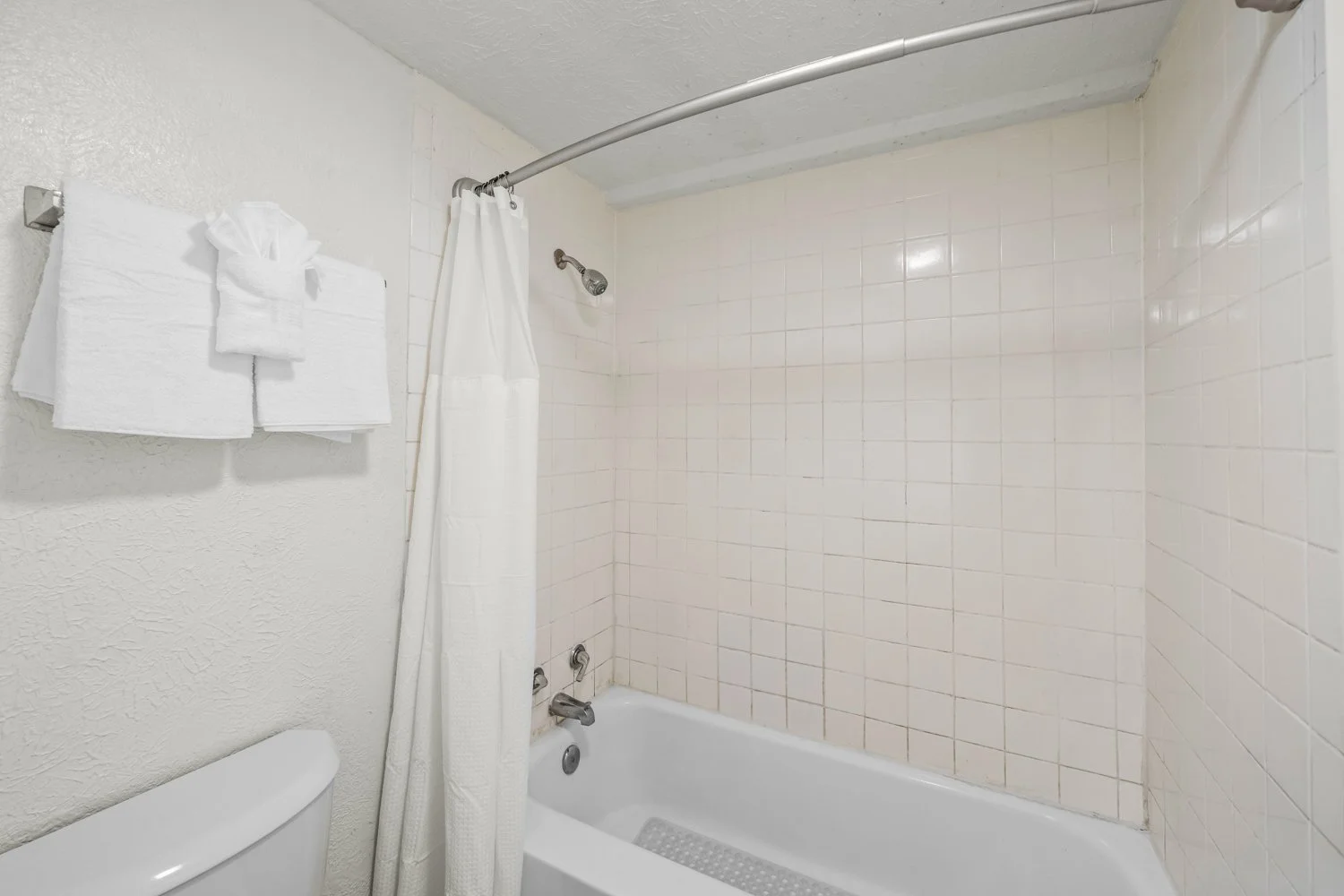 Empty bathroom with bathtub, shower head, curtain, towel rack with folded white towels, and beige tiled walls.