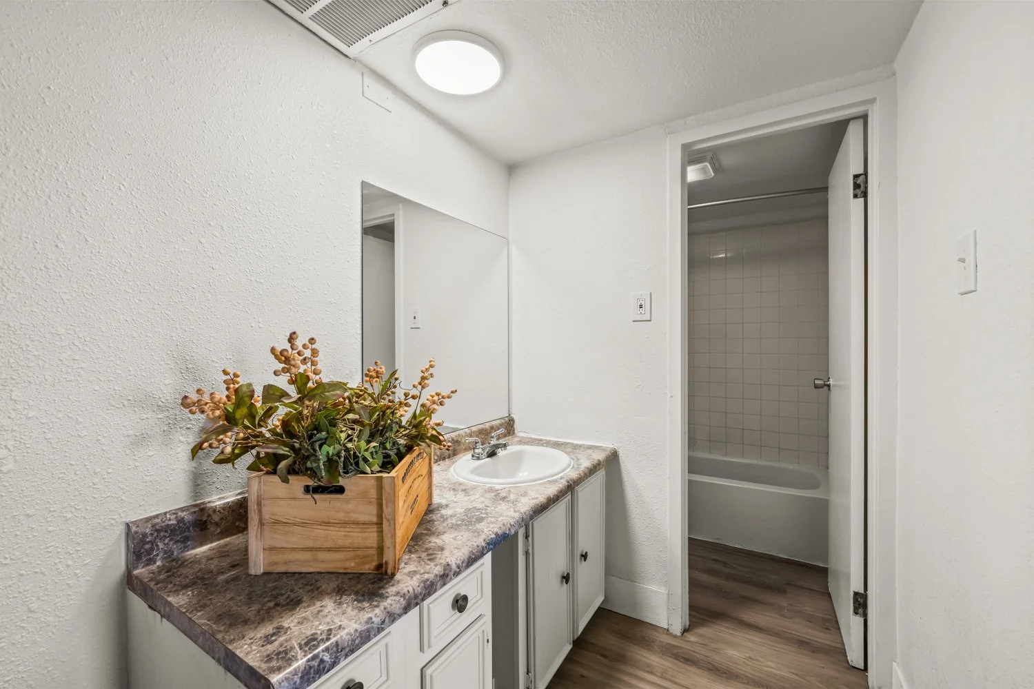 Bathroom with a small sink and countertop, and a closed door leading to a shower area with white tiles and bathtub.