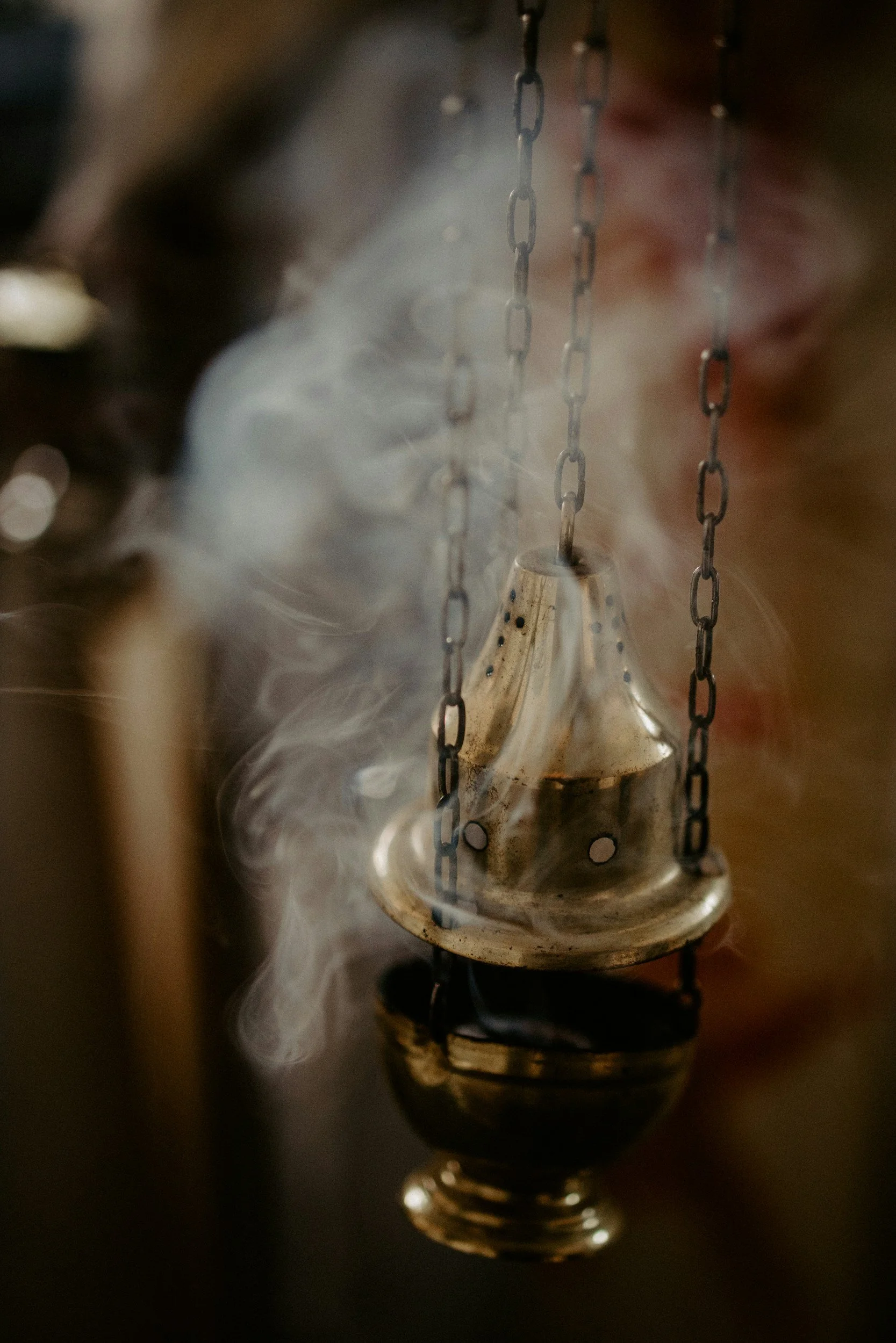 A small, metallic incense holder hanging from chains with smoke rising from it.