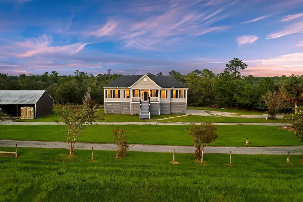 A raised Lowcountry home lit up at dusk on open fields