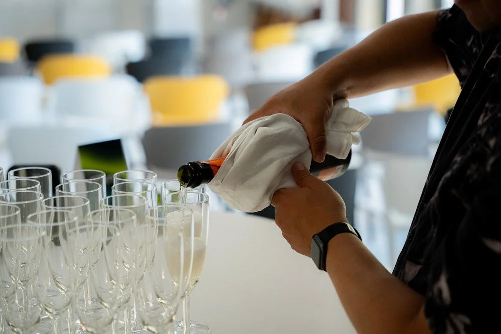 Eine Person füllt Champagner in Gläser in einem Saal.
