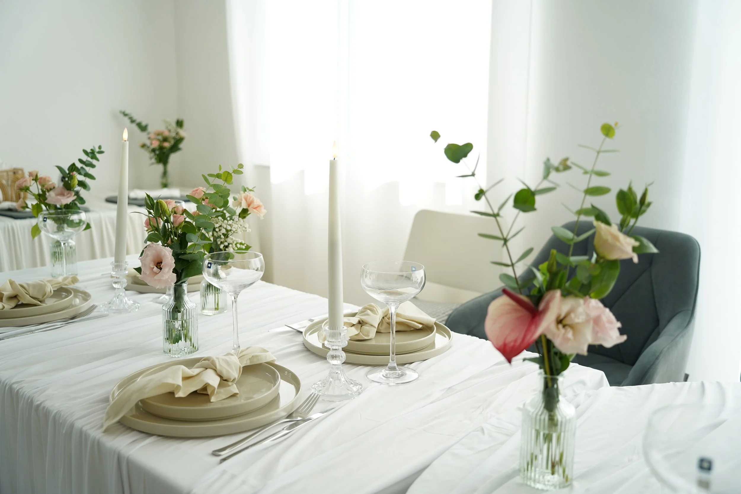 Ein eleganter festlich gedeckter Tisch mit Blumen, Kerzen und Geschirr in einem hellen Raum.