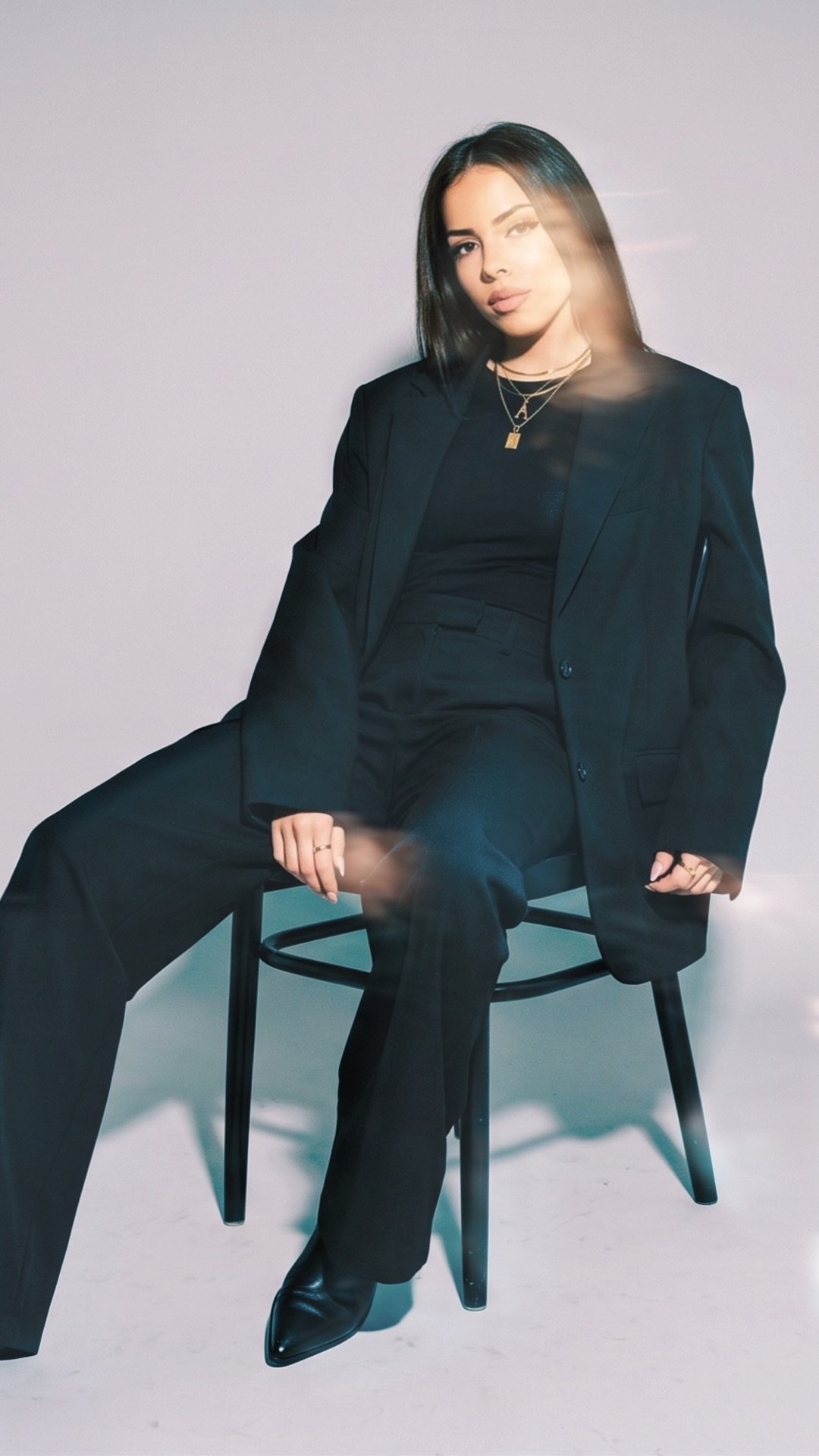 Junge Frau in schwarzem Anzug sitzt auf einem Stuhl vor einem grauen Hintergrund in einem Fotostudio.