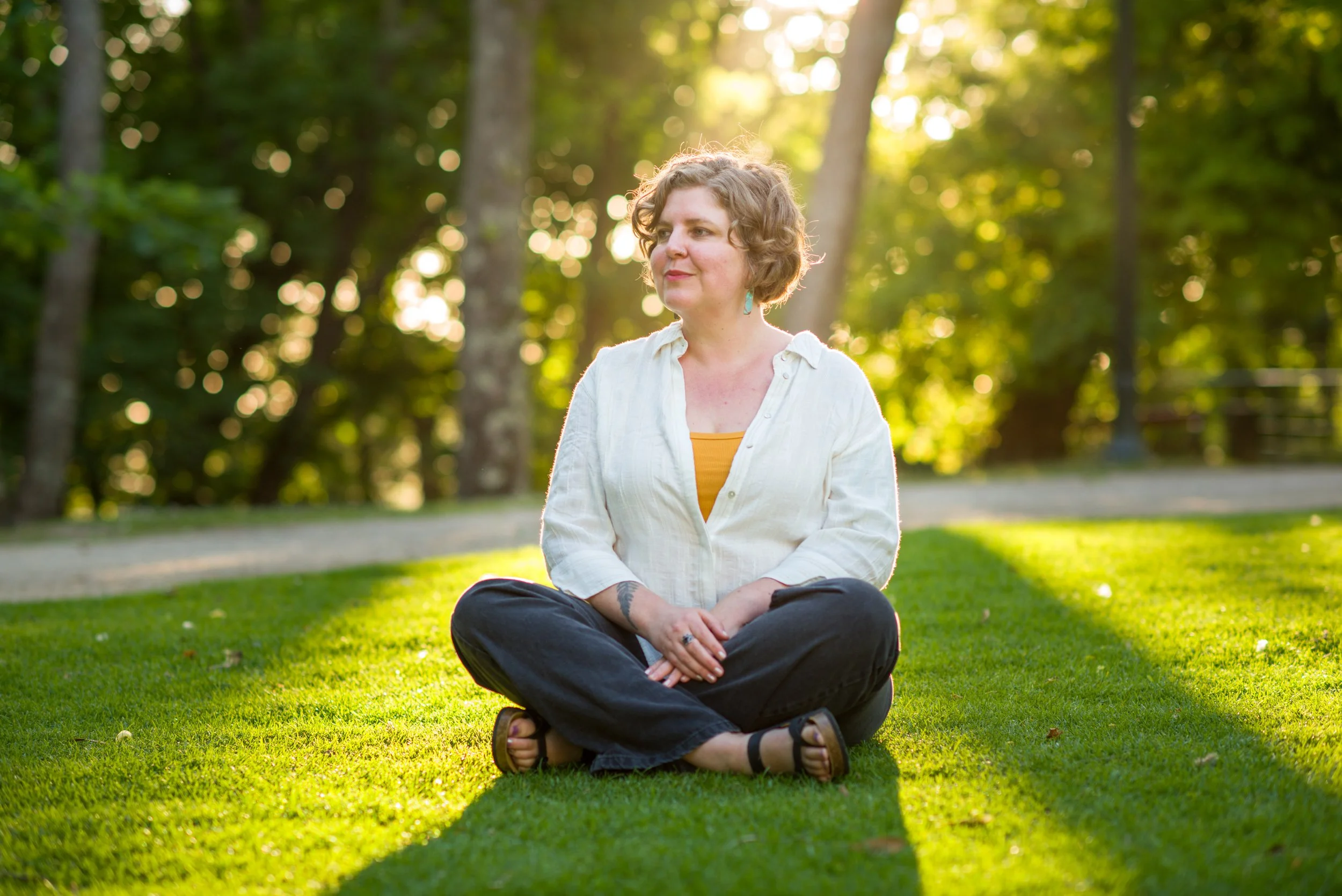 Chelsea Sokolow, LCSW, sits in green grass during golden hour, looking to the side.