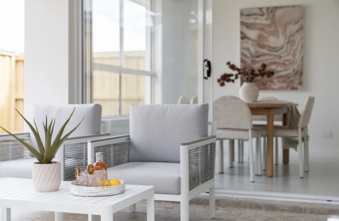 Bright, modern living and dining room with white furniture, potted plant, and abstract wall art.