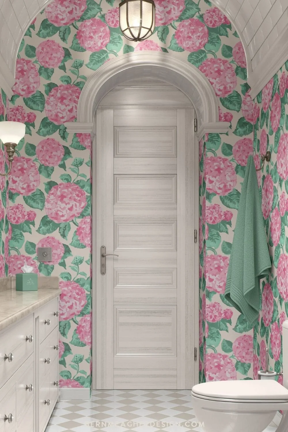 Pink and green hydrangea floral vinyl wallpaper covering all the walls of a narrow bathroom with a white arched door, white vanity with marble-look countertop, brass sconces, tiled barrel ceiling, mint towel, and white toilet on cream and white tiles
