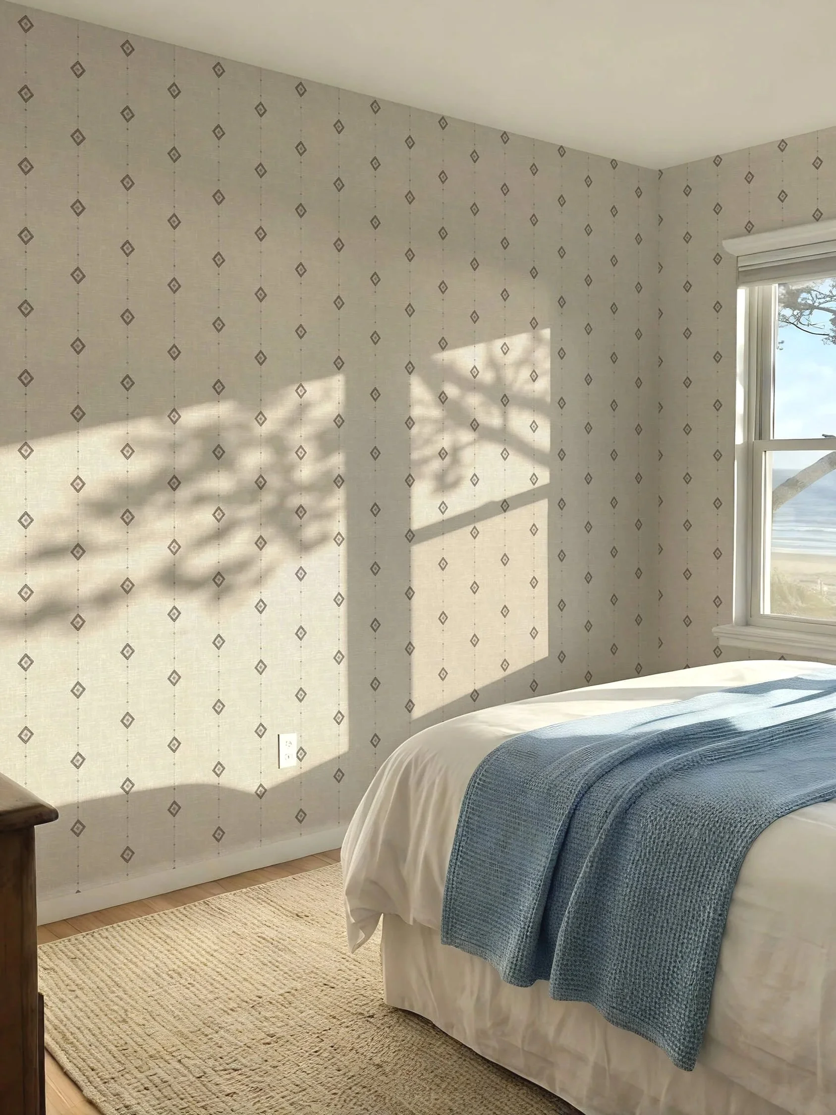 Relaxed hand drawn small diamonds featured on a cream textured wallpaper in a coastal bedroom with wooden floor and dresser, woven natural rug and blue blanket on white bed and natural sunlight through window showing a beach, giving a relaxed vibe.