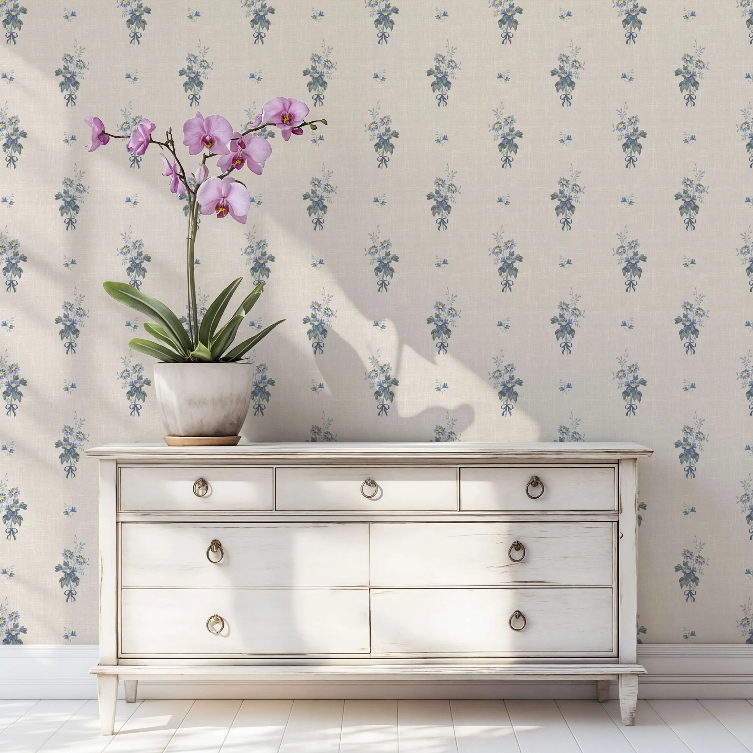 Vintage cottage style wallpaper with small blue wildflower bouquets on a beige linen-textured background, styled in a bright room with a white distressed wooden dresser and a potted orchid.