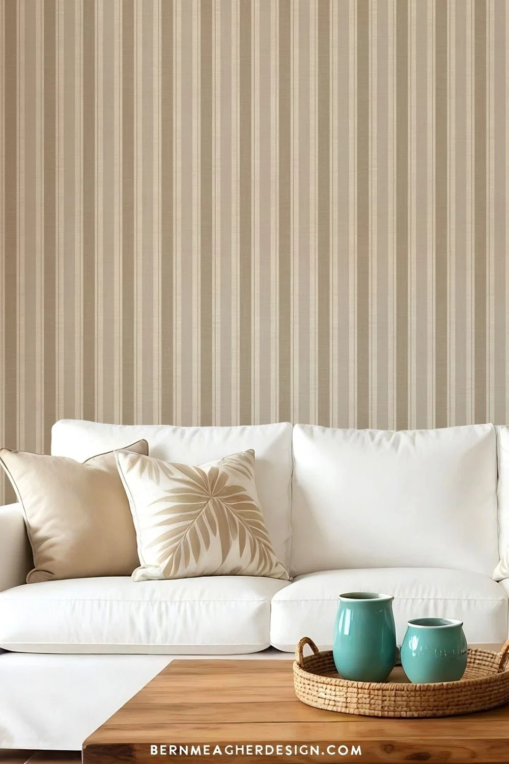 Striped khaki and beige peel and stick wallpaper on a living room accent wall, styled with a white sofa, white armchair, neutral patterned pillows, wooden coffee table, and dusty blue mugs
