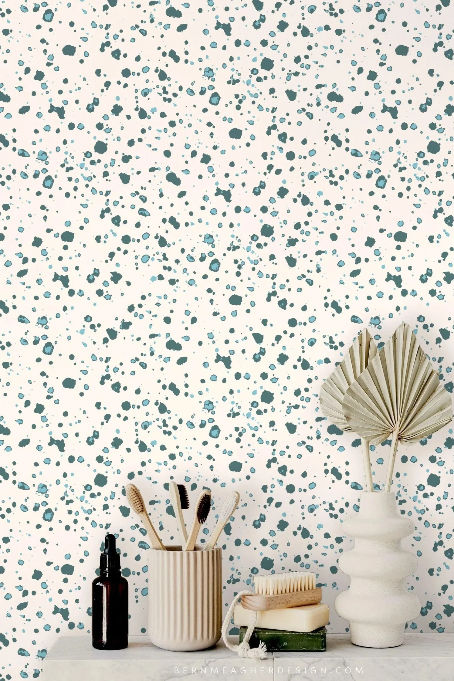 Blue and cream abstract ink splatter stone look vinyl wallpaper behind a marble bathroom shelf styled with neutral ceramic vessels, bamboo toothbrushes, a scrub brush, bar soap, and a sculptural white vase holding dried palm leaves.