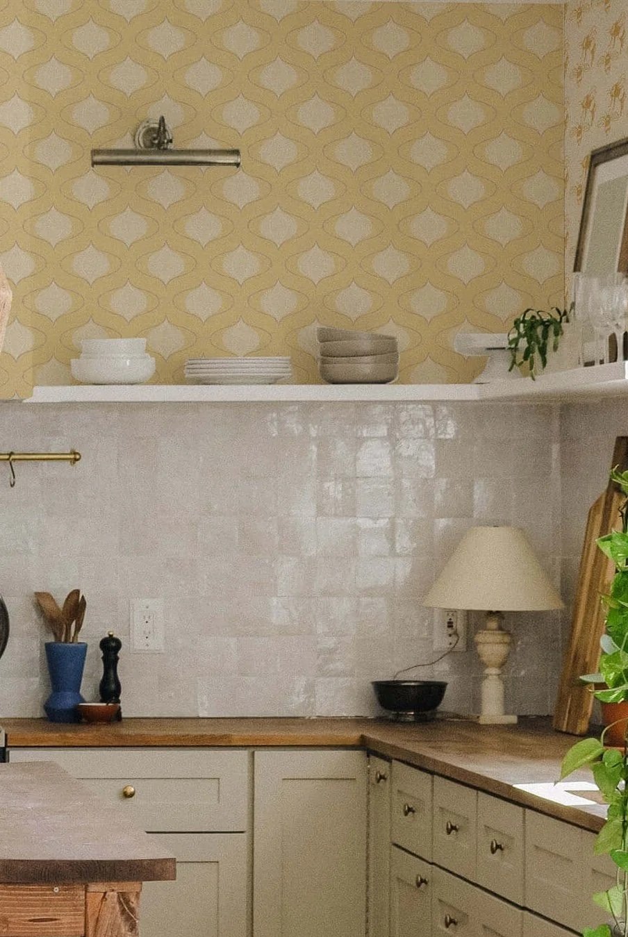 Farmhouse peel and stick wallpaper in warm butter yellow with a sweet vintage ogee pattern, showcased in a cozy kitchen featuring natural wood stools, a wooden island, cream cabinetry, and copper cookware hanging on the wall.