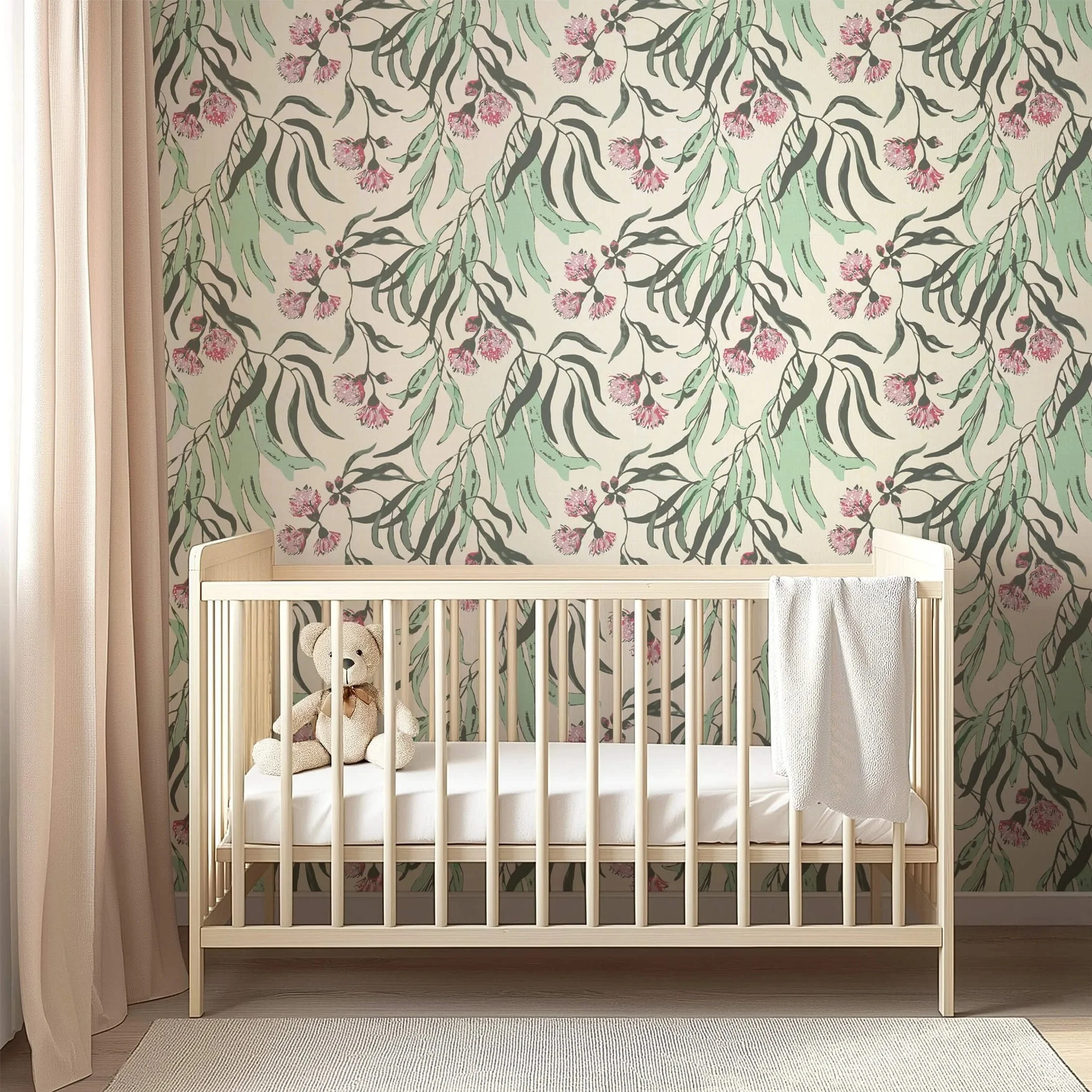 Wallpaper featuring a modern botanical style with soft green eucalyptus-like leaves and pink blossom clusters on a creamy yellow background behind a light wood crib and neutral curtains in a nursery setting.