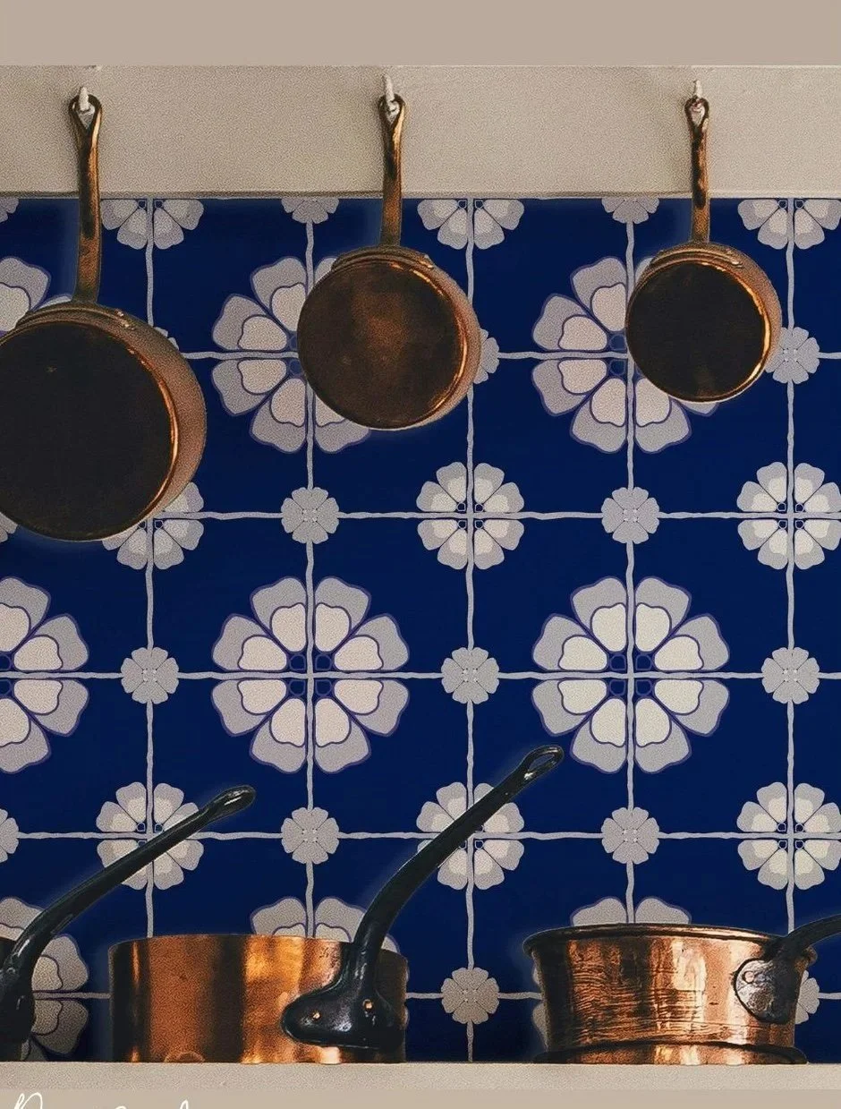 Copper pots hanging on a wall with blue and white patterned faux tiles wallpaper behind them.