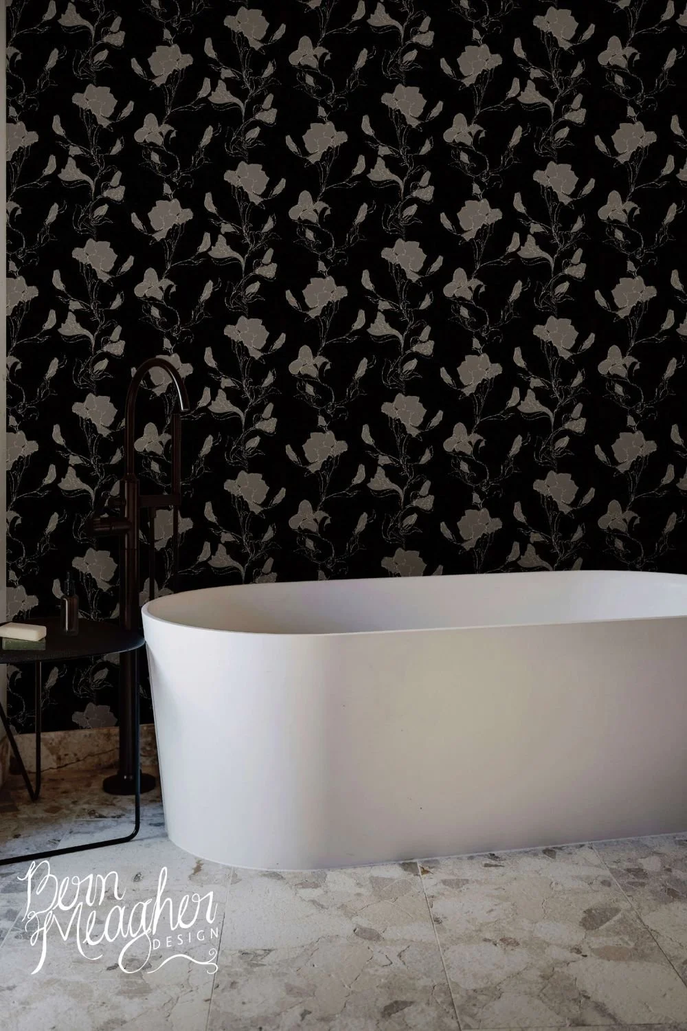 Modern bathroom with a white freestanding tub and black and gold floral peel and stick wallpaper on the wall, featuring subtle gold iris flowers on a black background with minimalist black fixtures and light stone flooring.