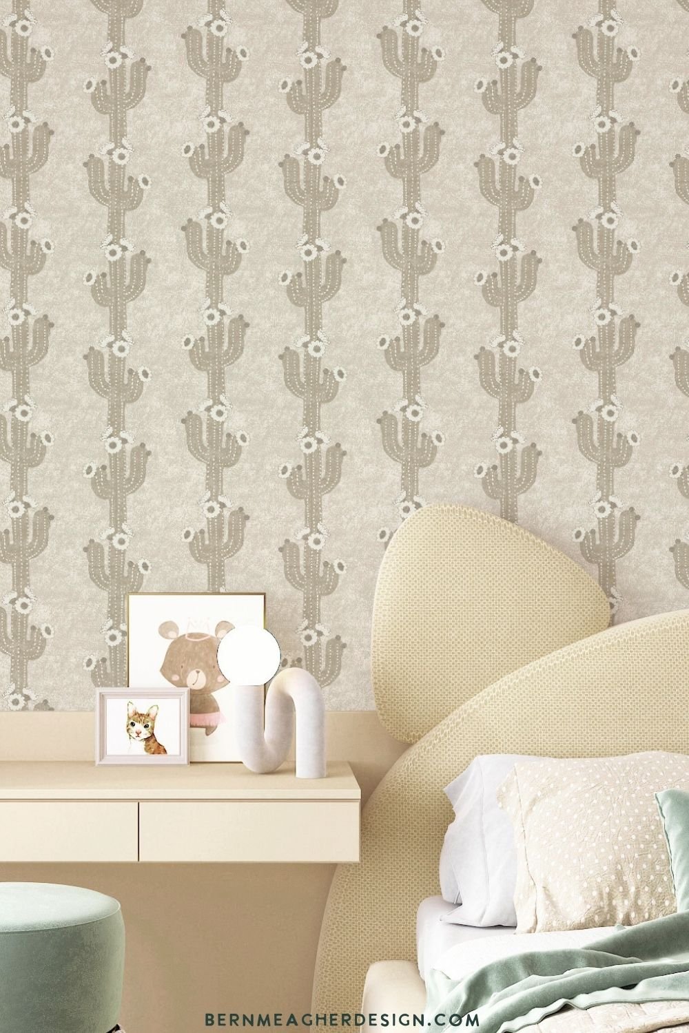 Peel and stick wallpaper with a vertical khaki beige cactus pattern on a light beige background, installed on a bedroom or study wall behind a minimalist cream desk, framed animal art, a small table lamp, and a round mint and white upholstered stool.