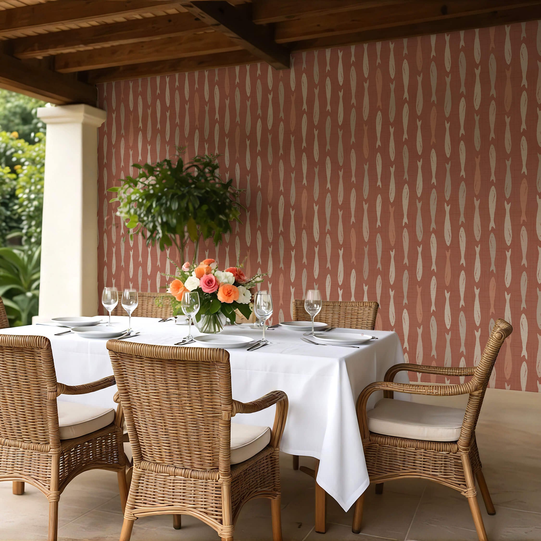 Peel and stick wallpaper in warm terracotta with a repeating sardine fish pattern, styled in an outdoor dining area featuring natural wicker chairs, a white tablecloth, and floral centerpiece under a wooden pergola.