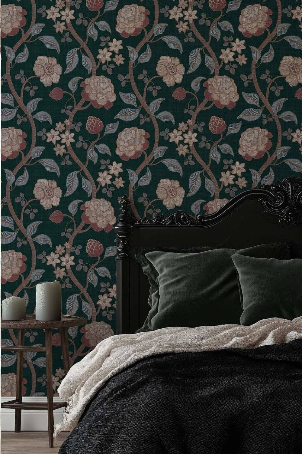 Dark teal green Victorian-style peel and stick wallpaper featuring intricate floral and leafy patterns displayed behind a black ornate bed with dark green velvet pillows and neutral bedding, alongside a wooden side table holding candles.