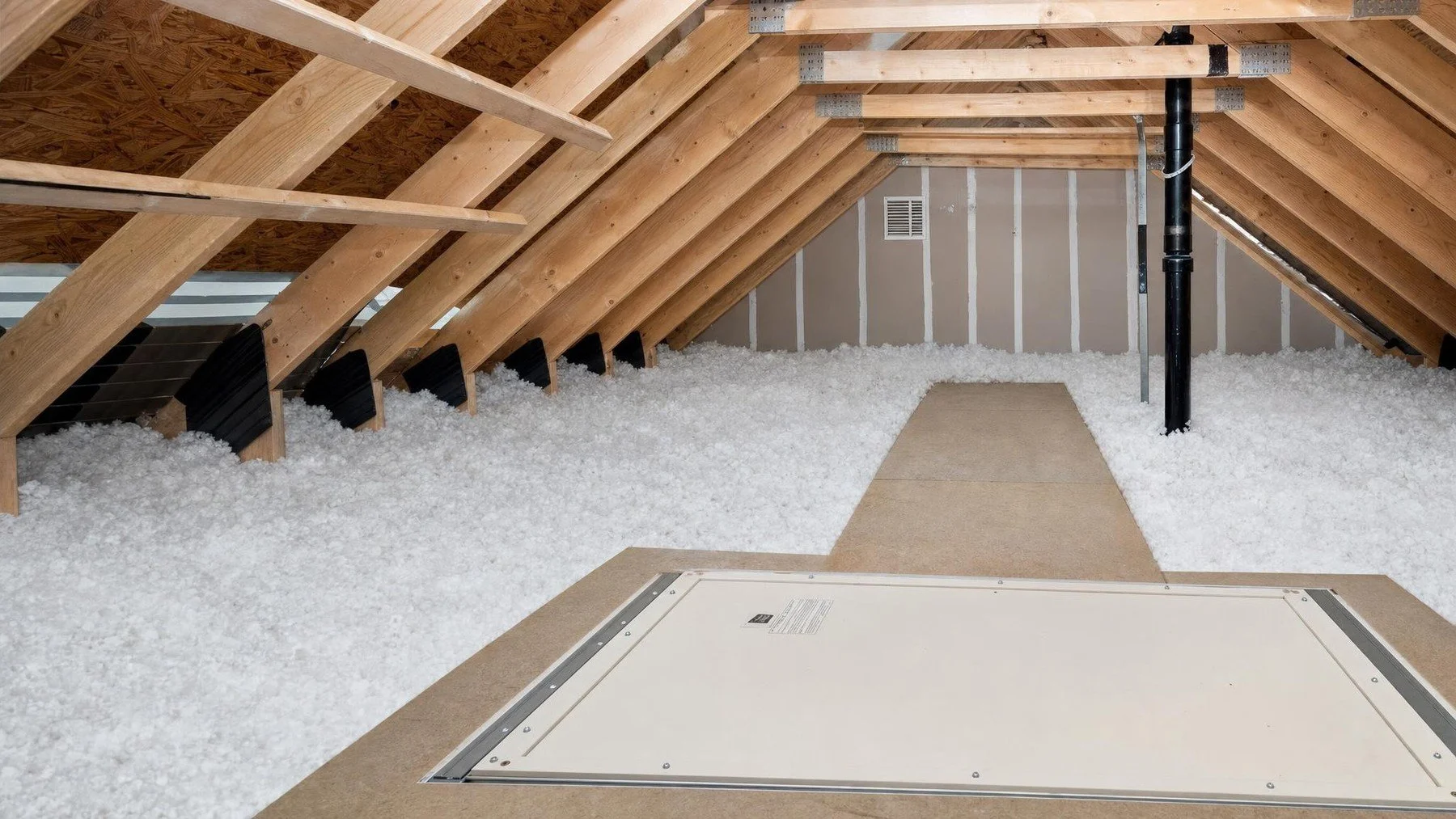 Attic with settled blown-in insulation between wood rafters beside a plywood access hatch and vent in an Oakville home