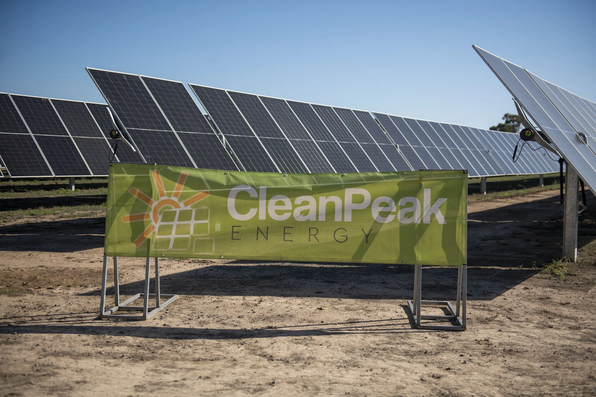 Solar panels behind a green banner that reads 'CleanPeak Energy' on a dirt lot.