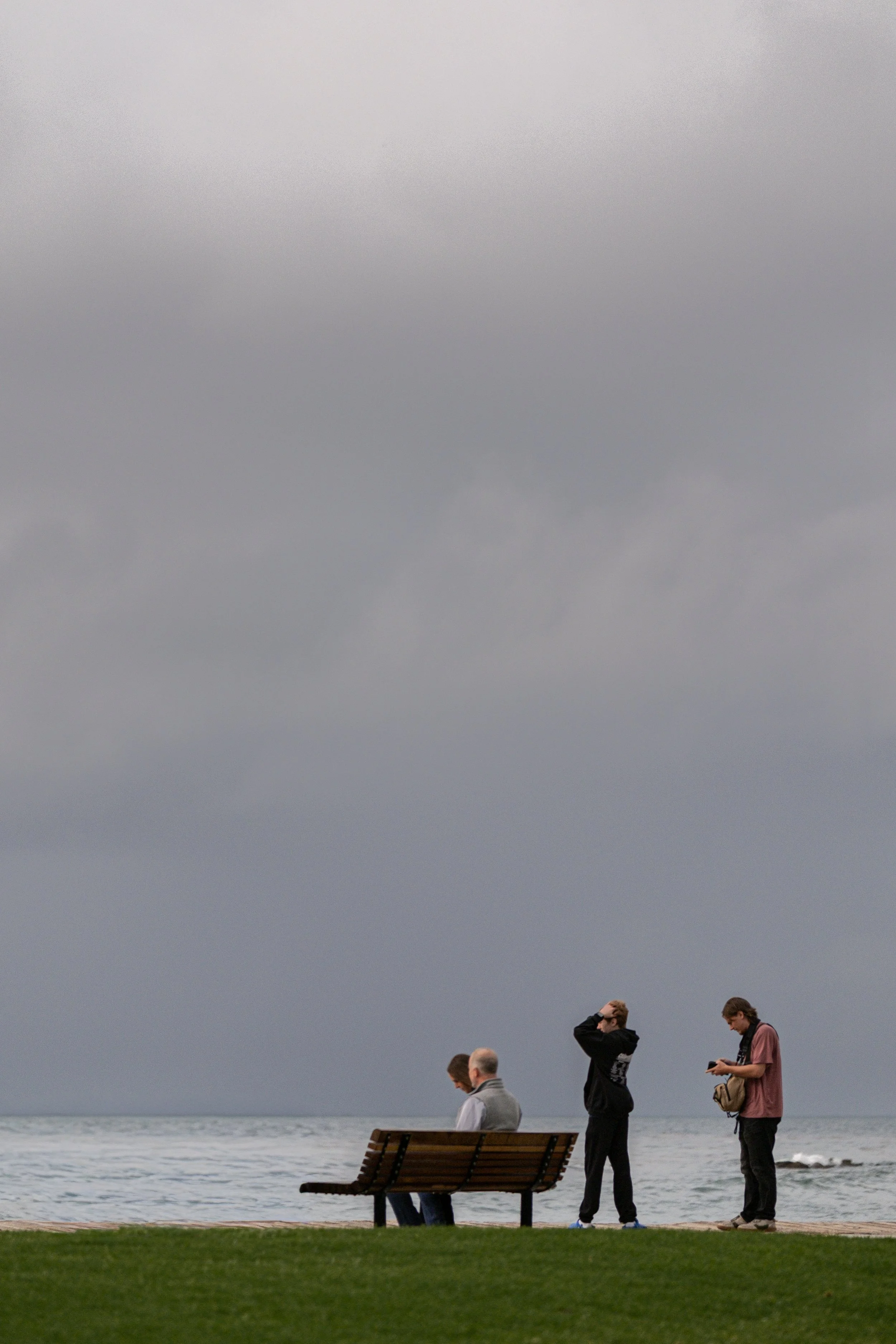  A quiet moment shared on a boardwalk bench, framed by the muted teals of the post-rain ocean. 