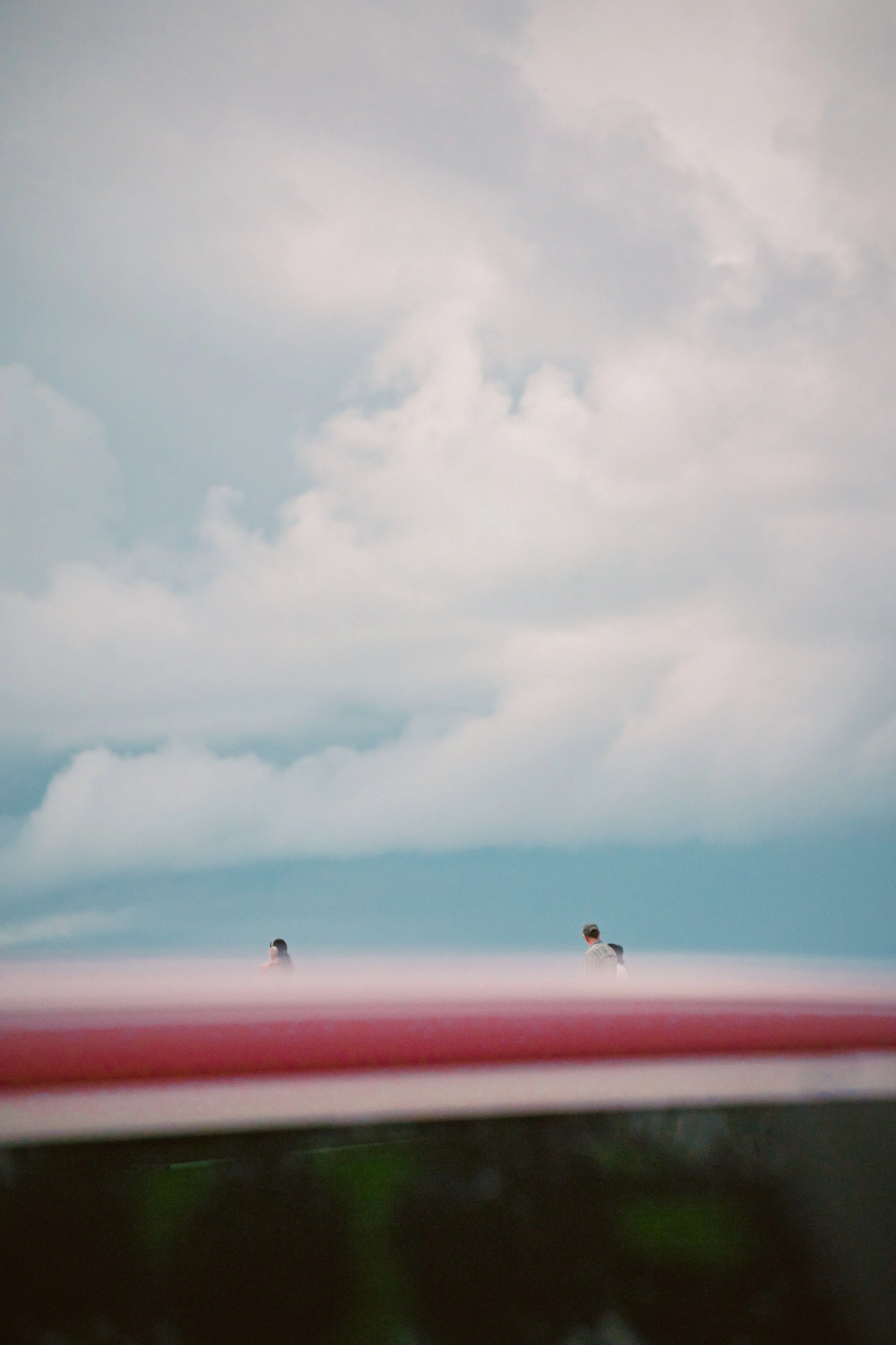  Two distant figures on the horizon appear as silhouettes where the grey sky meets the sea. a Red car just drove by which ended up taking this photo.  