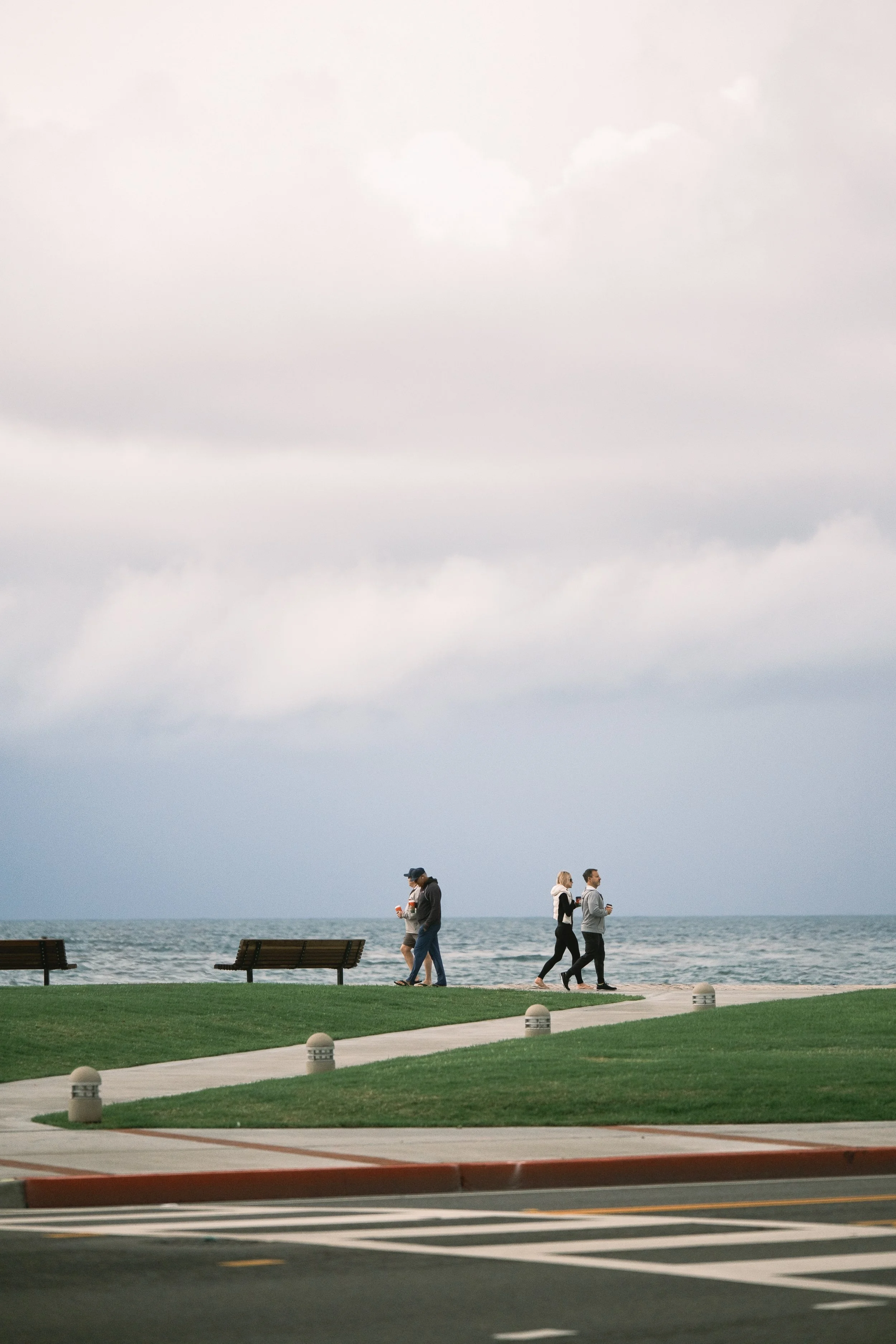 A wide, cinematic view of the boardwalk path cutting through the damp green grass of Main Beach. 