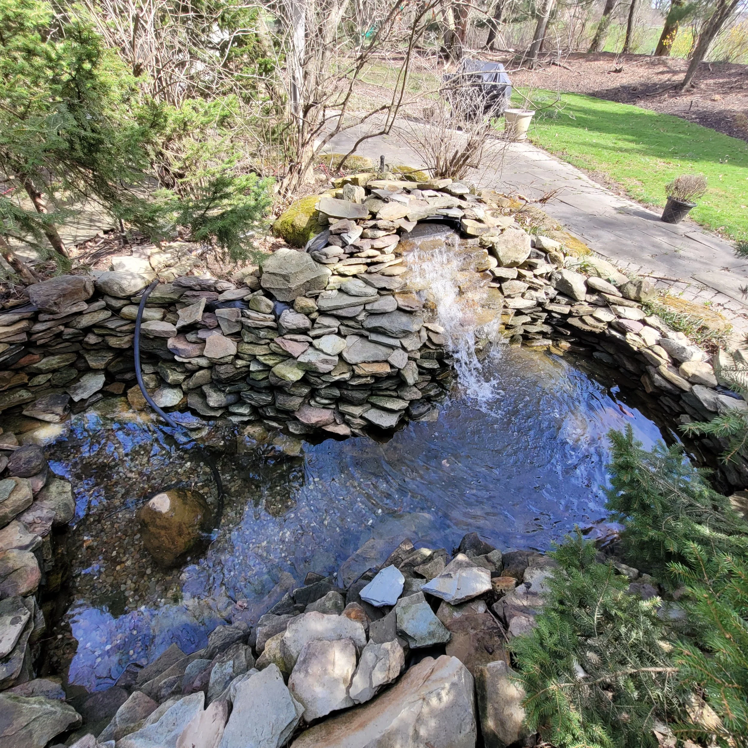 Stone waterfall feature in a small garden pond with surrounding greenery.