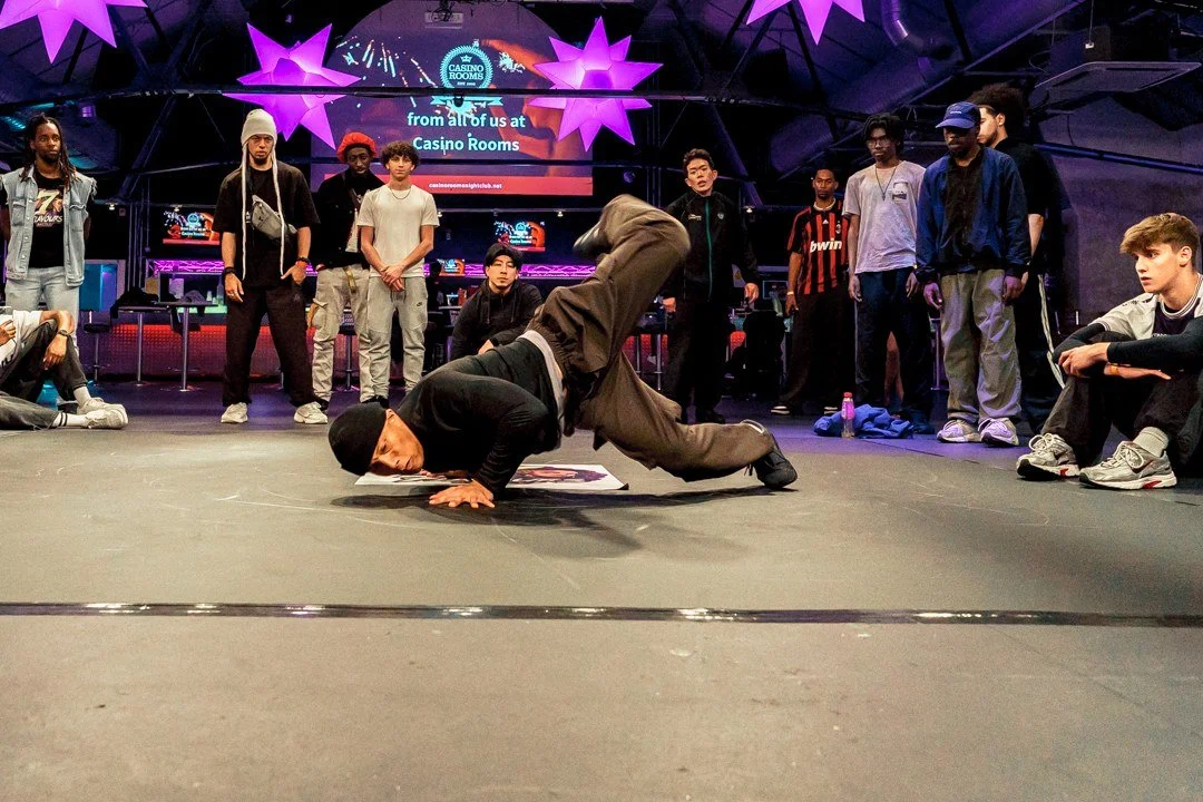 Breaking dancer performing floorwork in a USDD dance battle, surrounded by the dance community under purple stage lights.