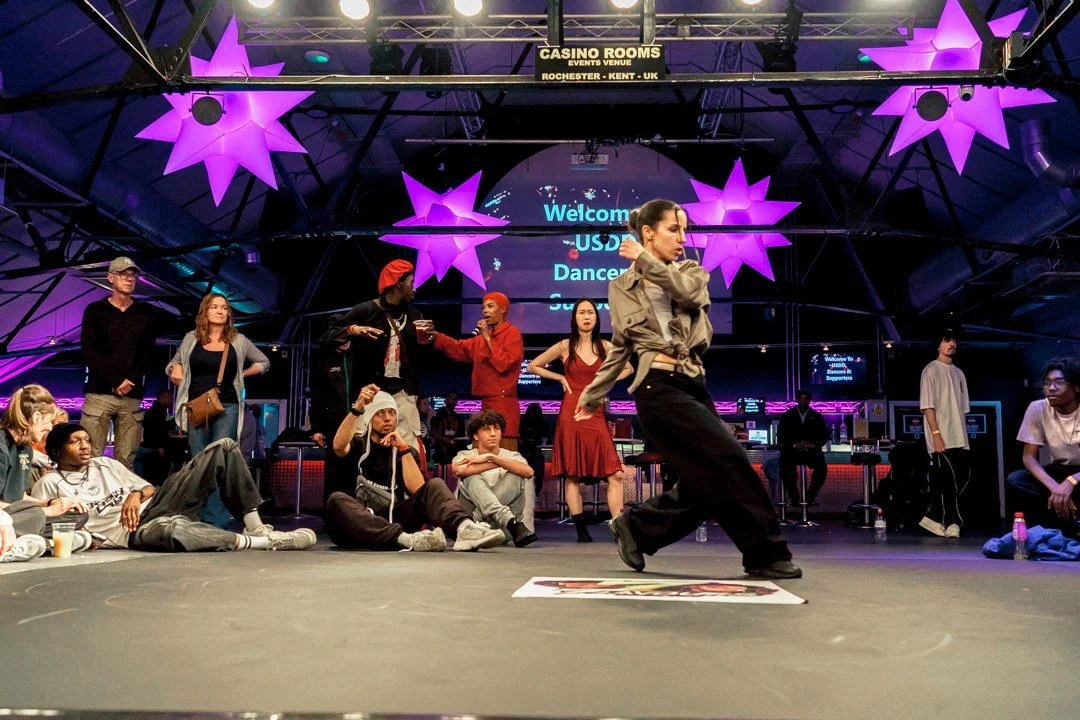 Freestyle dance performance at a USDD event, with spectators around the dancer under purple lights.