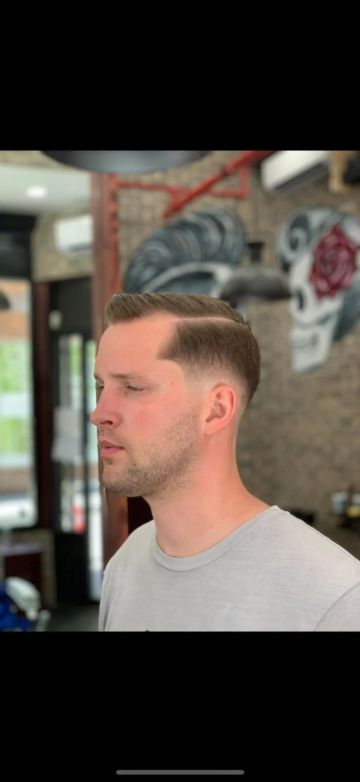 Side profile of a man with a freshly styled haircut, featuring short sides and combed top, inside a barbershop with exposed brick walls and artwork.