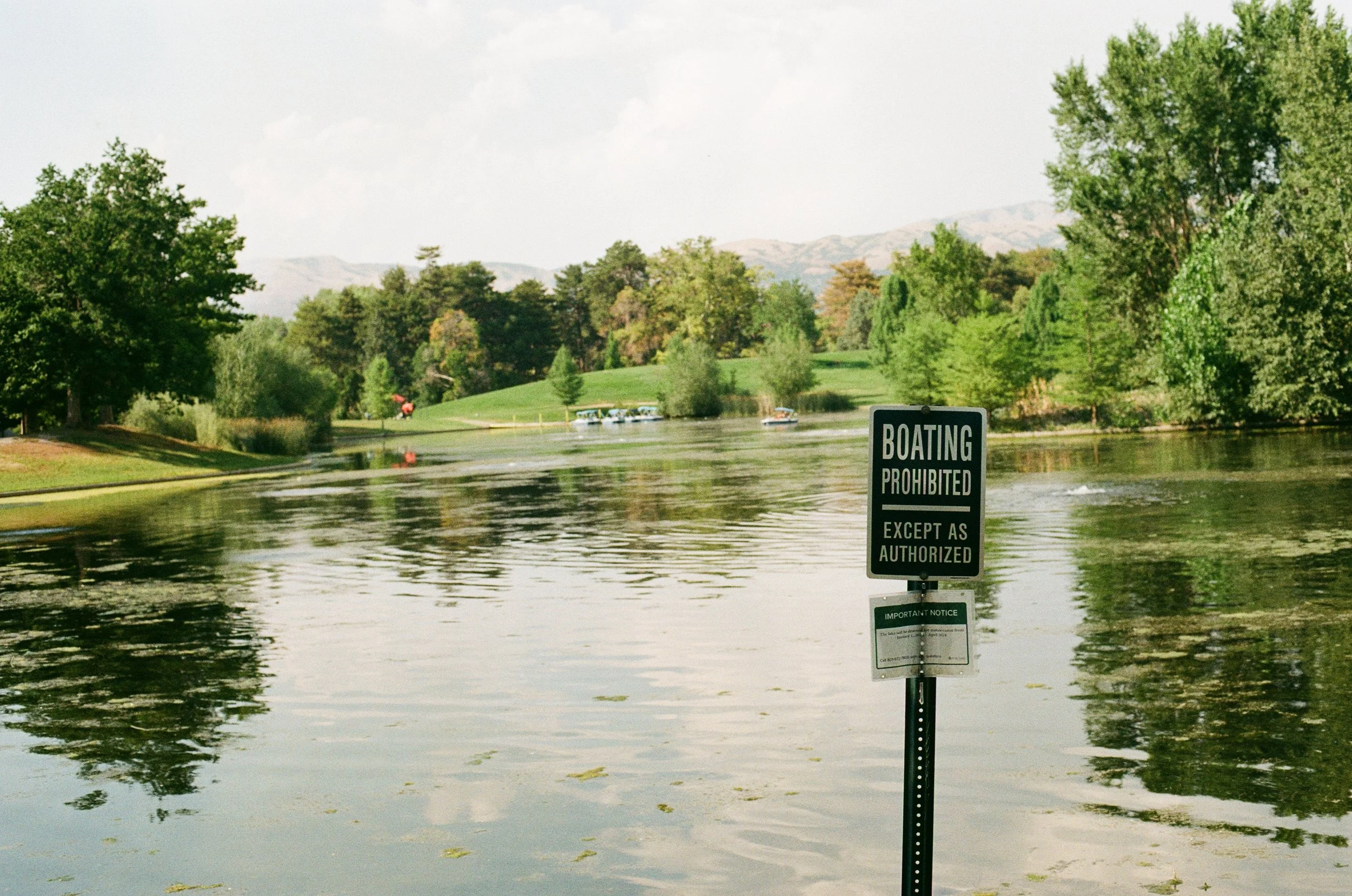 A lake with green trees and mountains in the background, with a sign that says 'Boating Prohibited Except as Authorized' in the foreground.