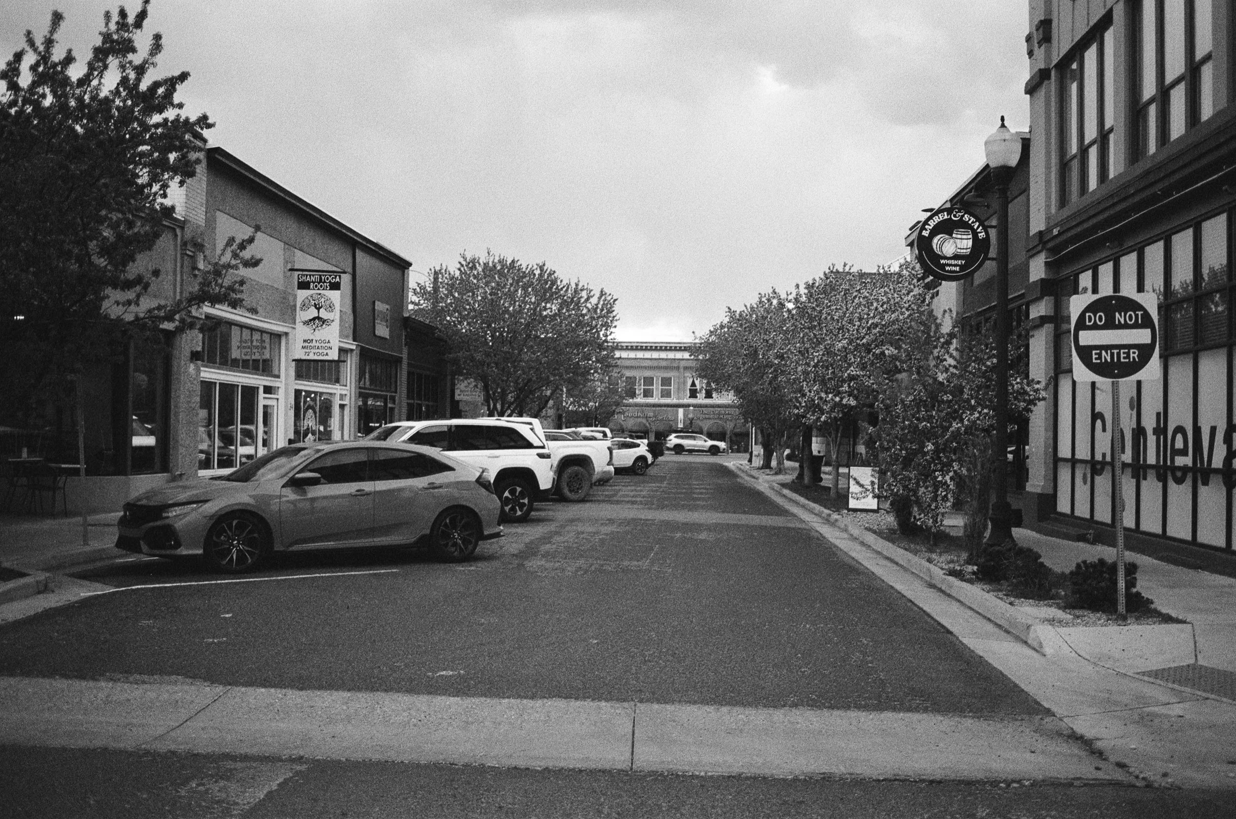 A small urban street scene with parked cars, trees, storefronts, and a 'Do Not Enter' sign on the right.