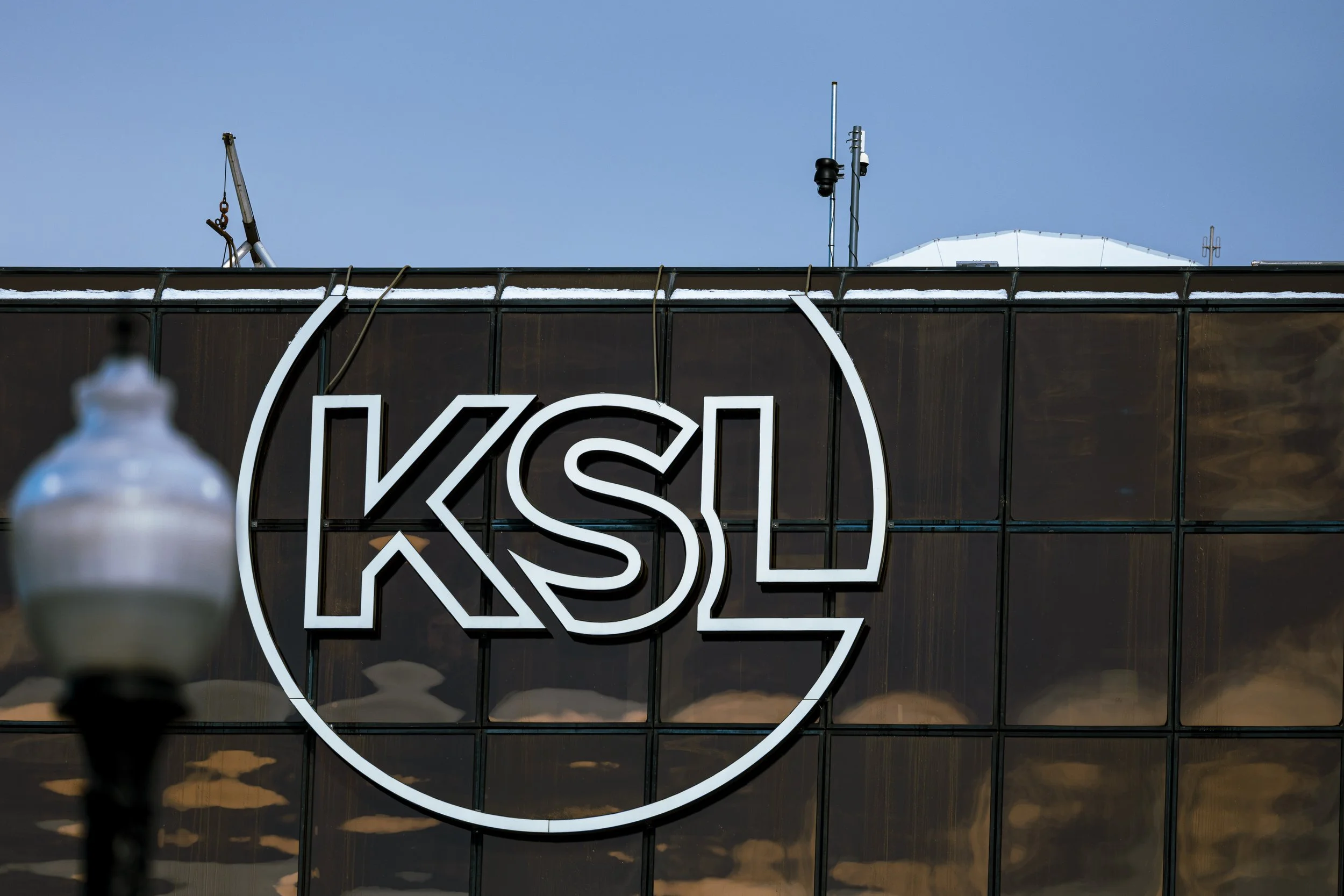 Close-up of a building's glass facade with a large circular logo that says 'KSL' in the center, with a blue sky in the background.