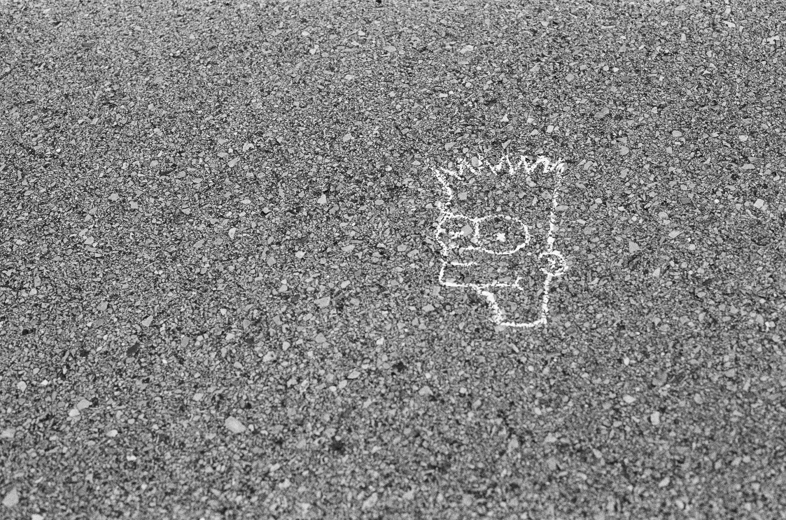 A small chalk drawing of a person's head and upper body on a gray asphalt surface.