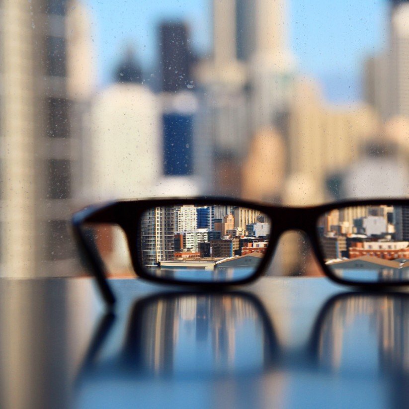 Pair of glasses sitting on a table facing a city skyline.