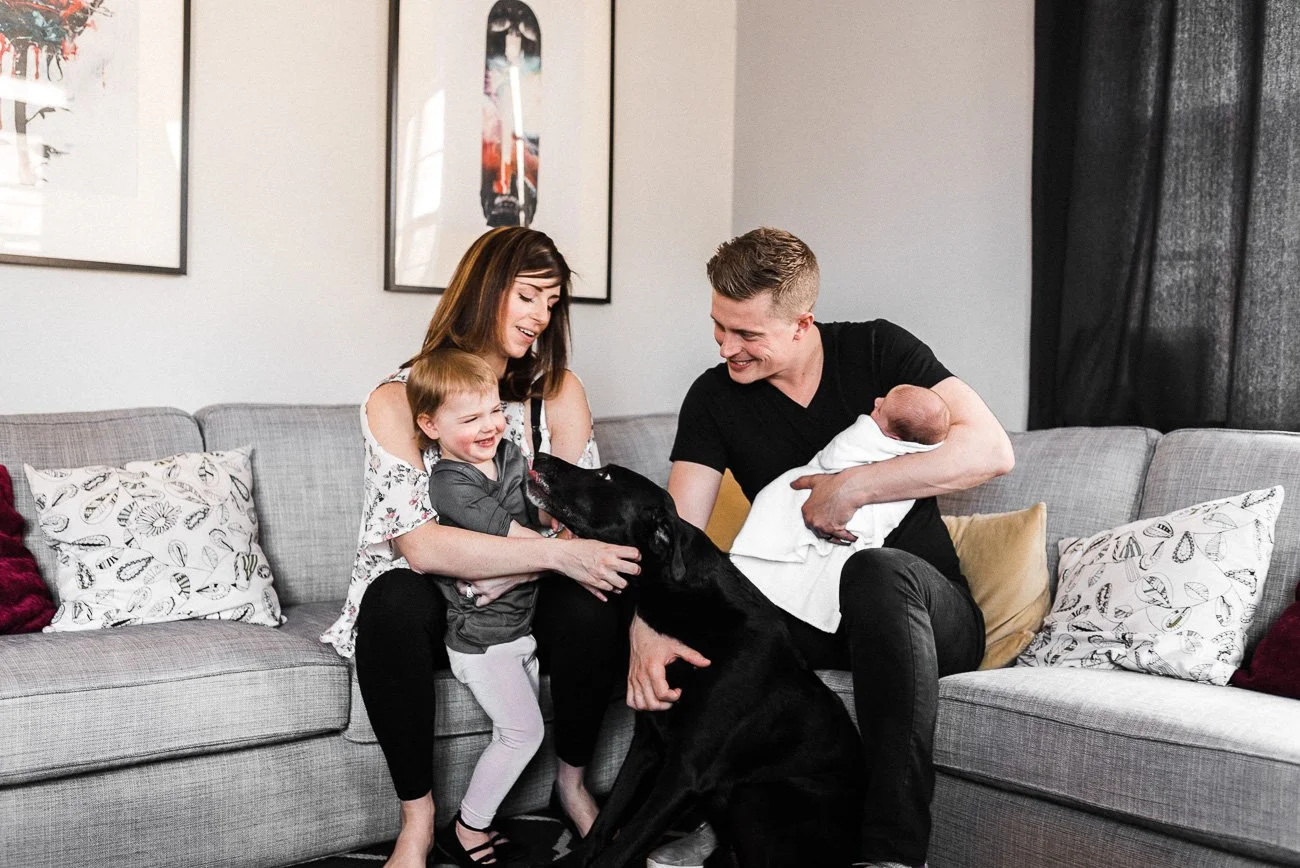 A happy family with a newborn and a toddler with their dog in the living room