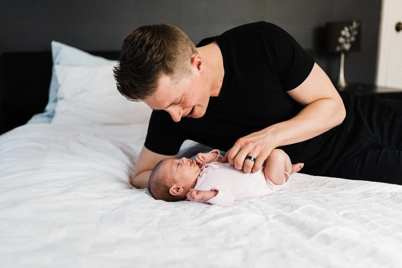 Photo of a new dad having cuddly time with his newborn in the bed