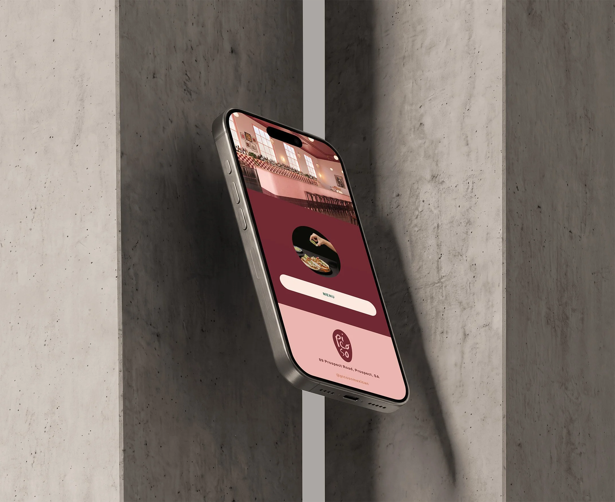 Smartphone resting on gray concrete surface displaying a restaurant or food-related app with a menu, contact information, and social media handle.