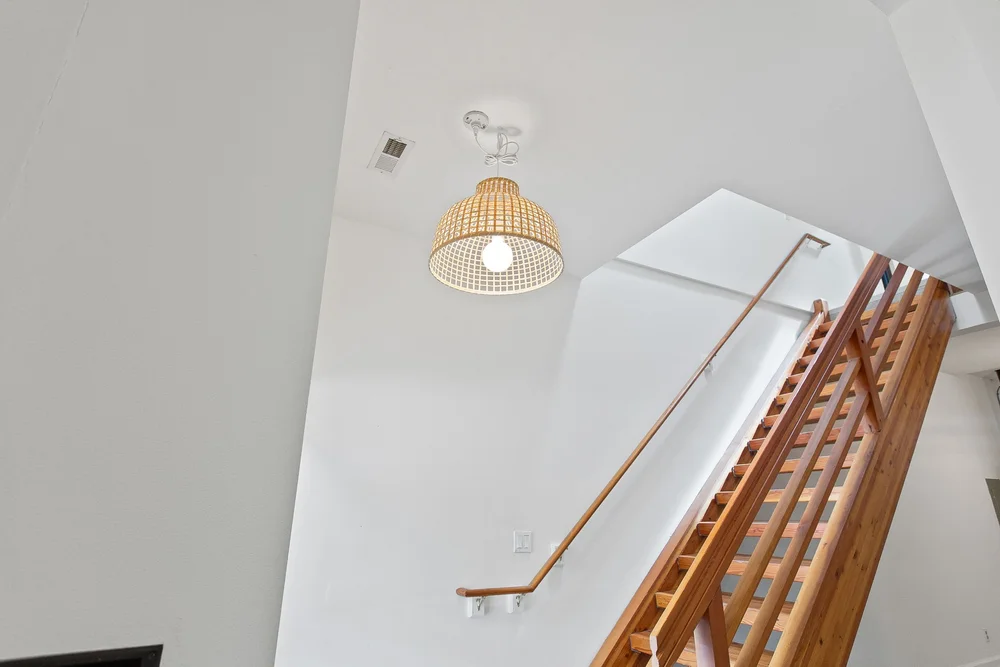 Bright interior stair with a wood handrail and a woven pendant light