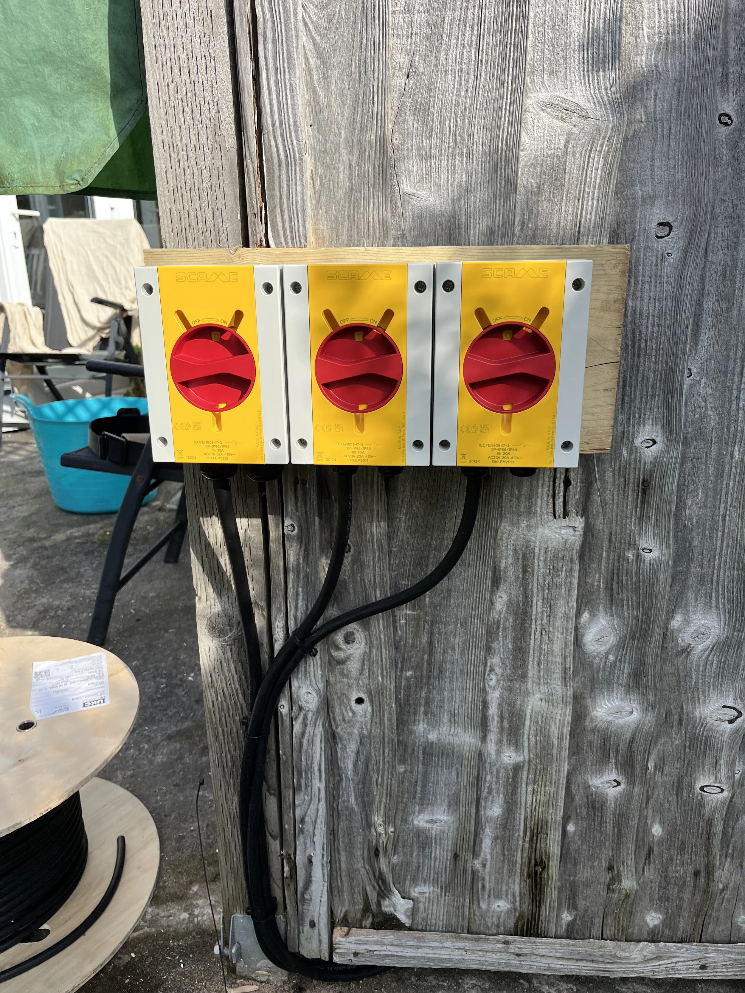 Three yellow and red electrical rotary switches mounted on a wooden panel, with black cables running below.