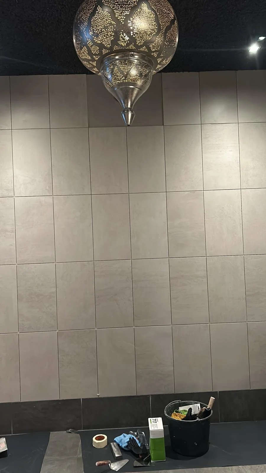 Lange, smalle gang met witte muren, donkere vloer en plafondlamp.