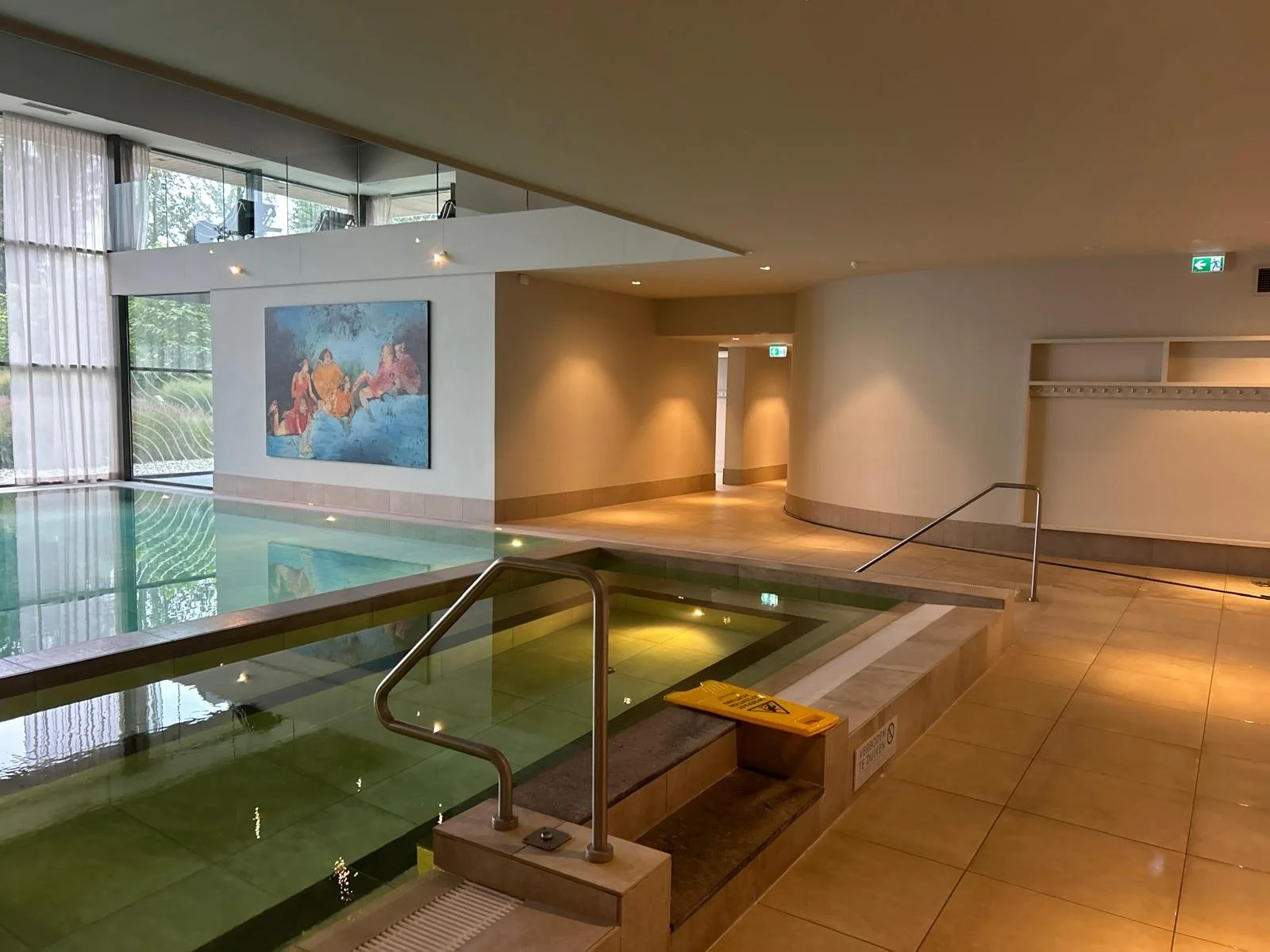 Een hoog appartementencomplex met een rode bakstenen gevel en meerdere rijen ramen. De ingang heeft een glazen deur en een aantal brievenbussen. Een persoon staat binnen.