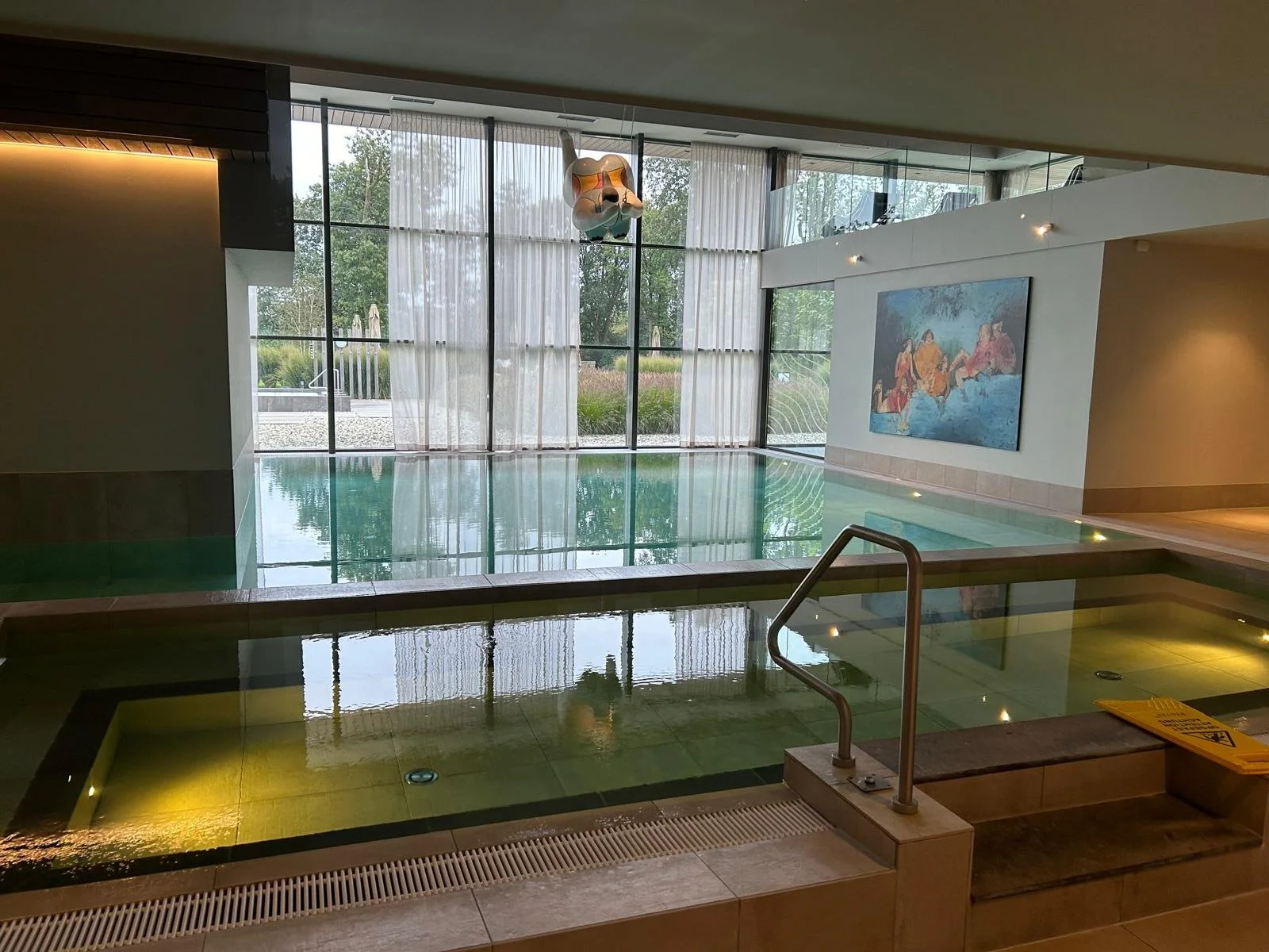 De gevel van een gebouw met een glasdeuren ingang, een bord met bedrijfsnaam singel en contactgegevens, en enkele mensen binnen die werken.