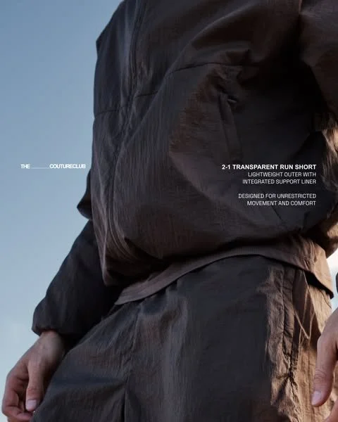 Close-up of a person wearing a black urban outdoor jacket and pants, with text mentioning a 2-in-1 transparent run short with lightweight outer and integrated support liner.
