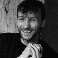 Smiling person with short hair, wearing an earring, in a black and white photo.