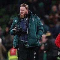 Man in a green jacket holding a camera on a sports field